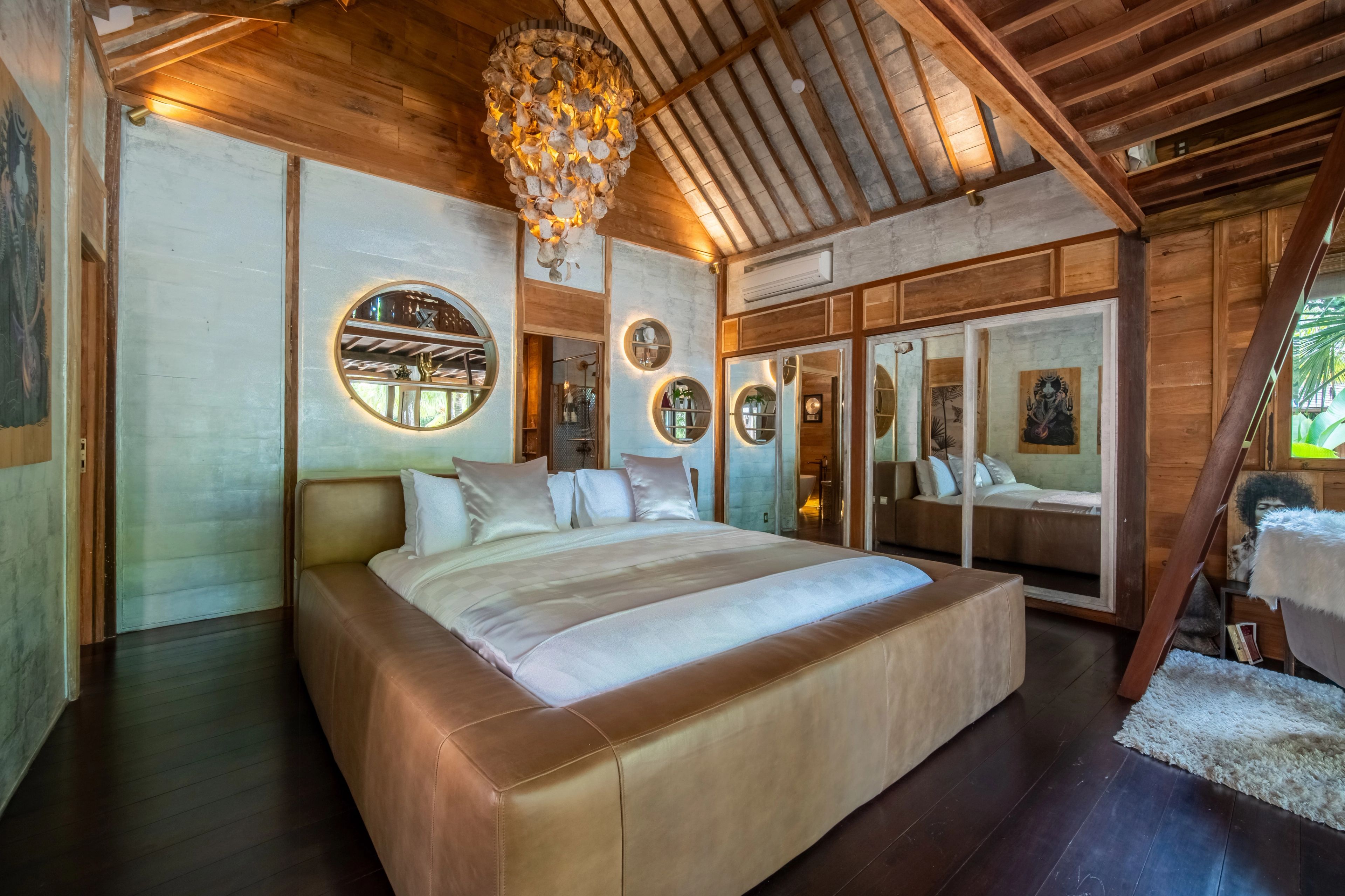 The leather-based bed under the shell chandelier, round mirrors and framed prints along the wall.