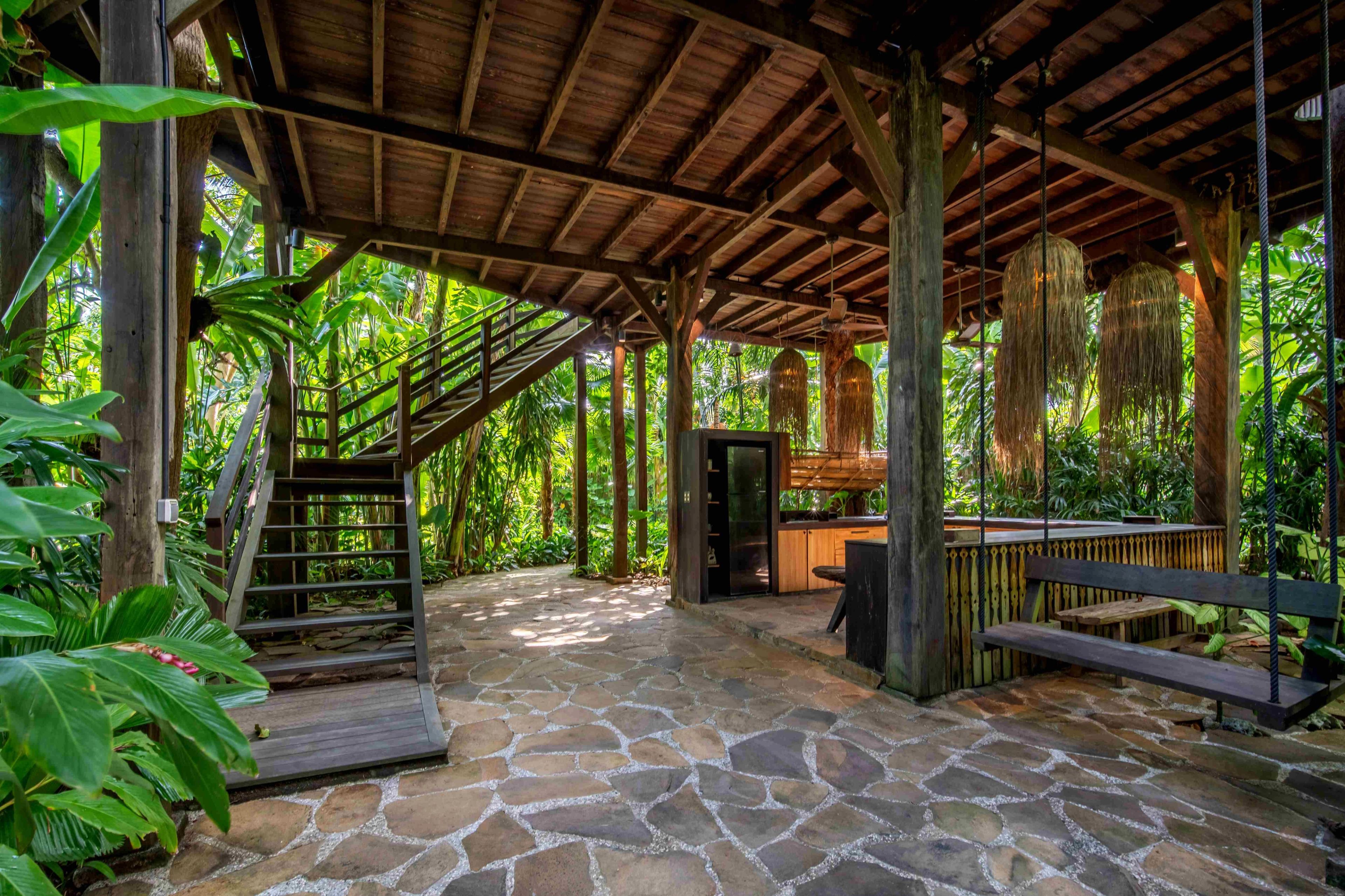 A flagstone terrace under the treehouse's timber frame, with the stair up and a long bench along one side.