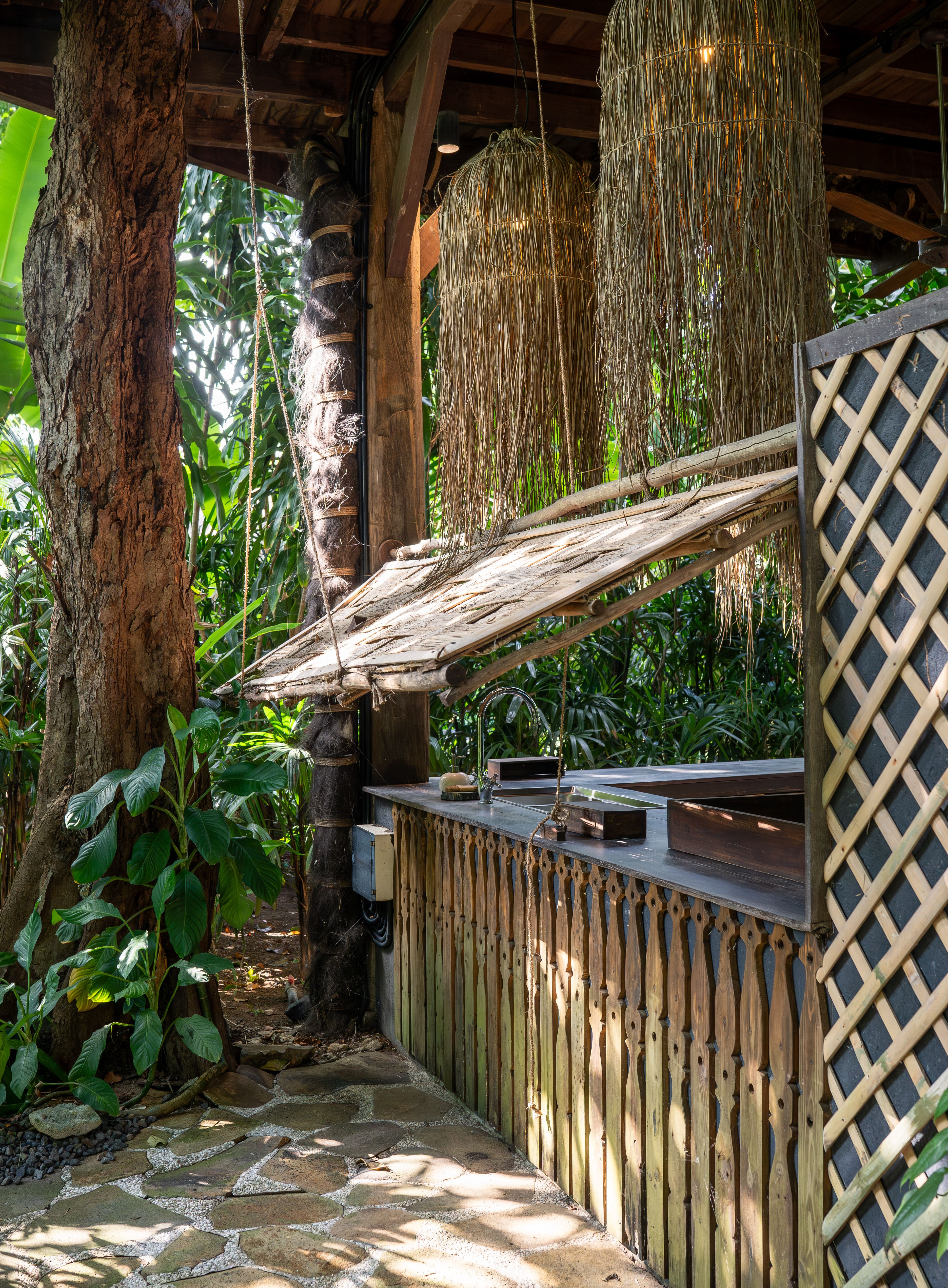 The outdoor kitchen counter built around a tree trunk, with a lattice screen and jungle beyond.