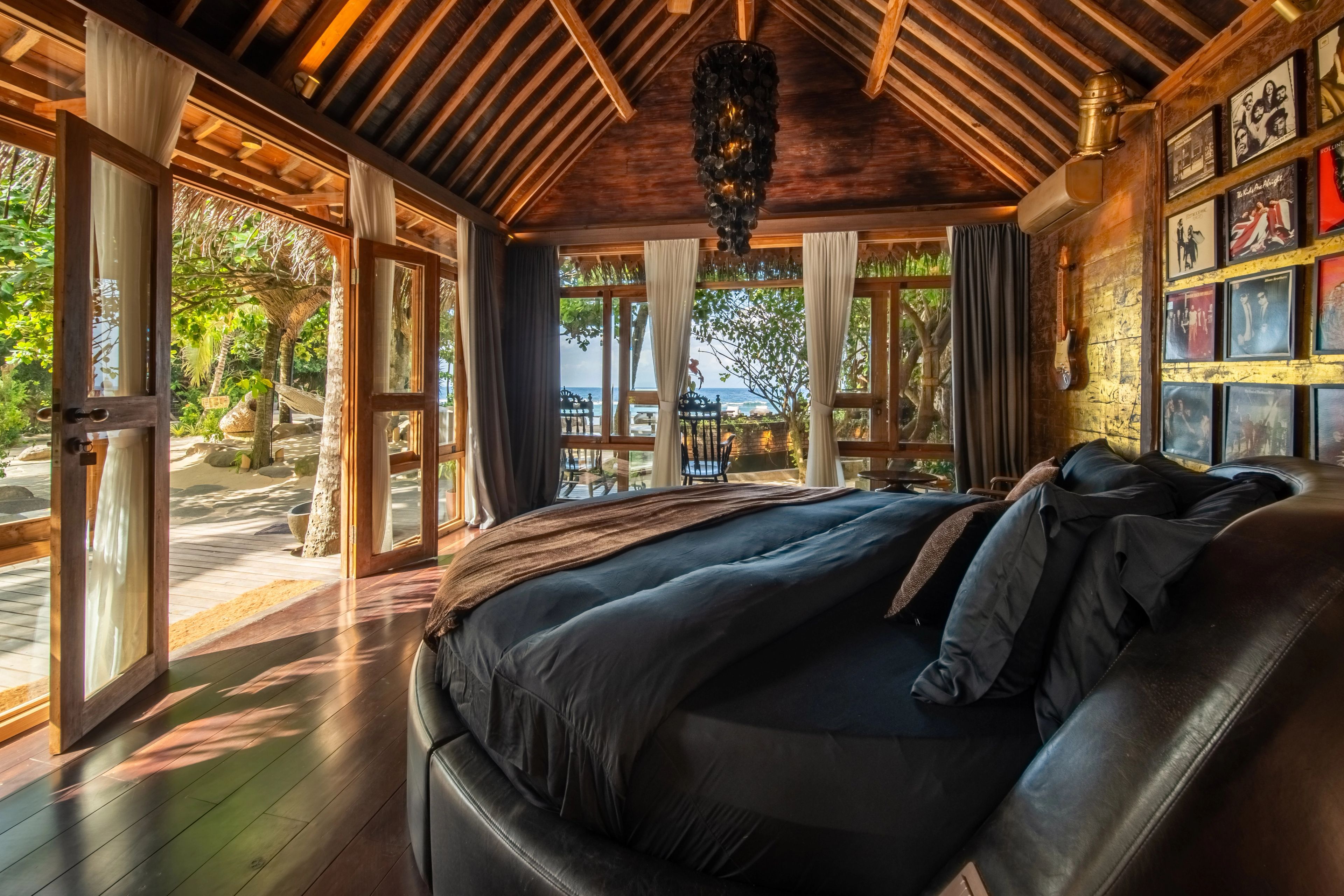 The circular bed in dark linen, doors folded back to the deck and the palms outside.