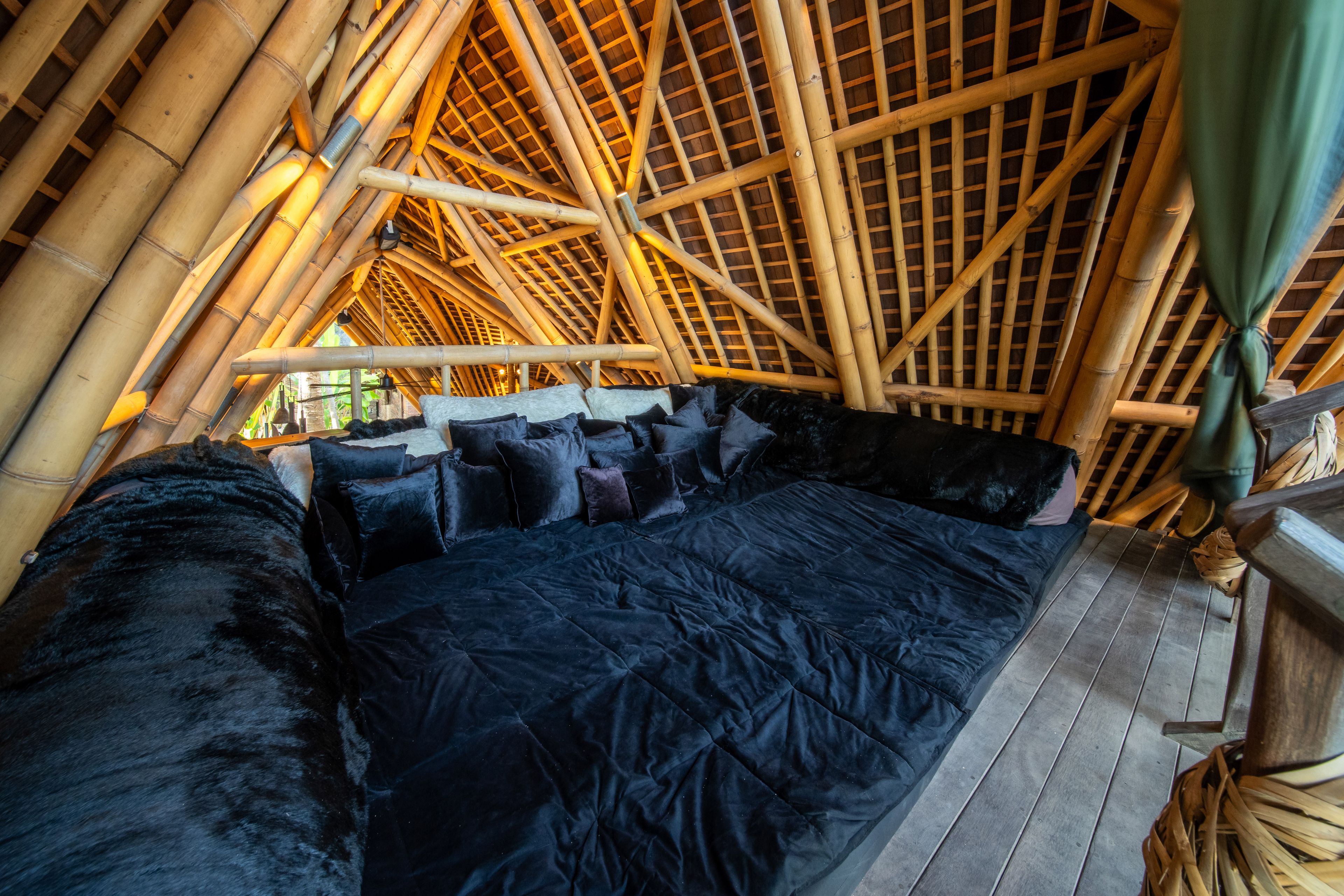 A bed made up in dark linen beneath the fanned bamboo structure of the roof.