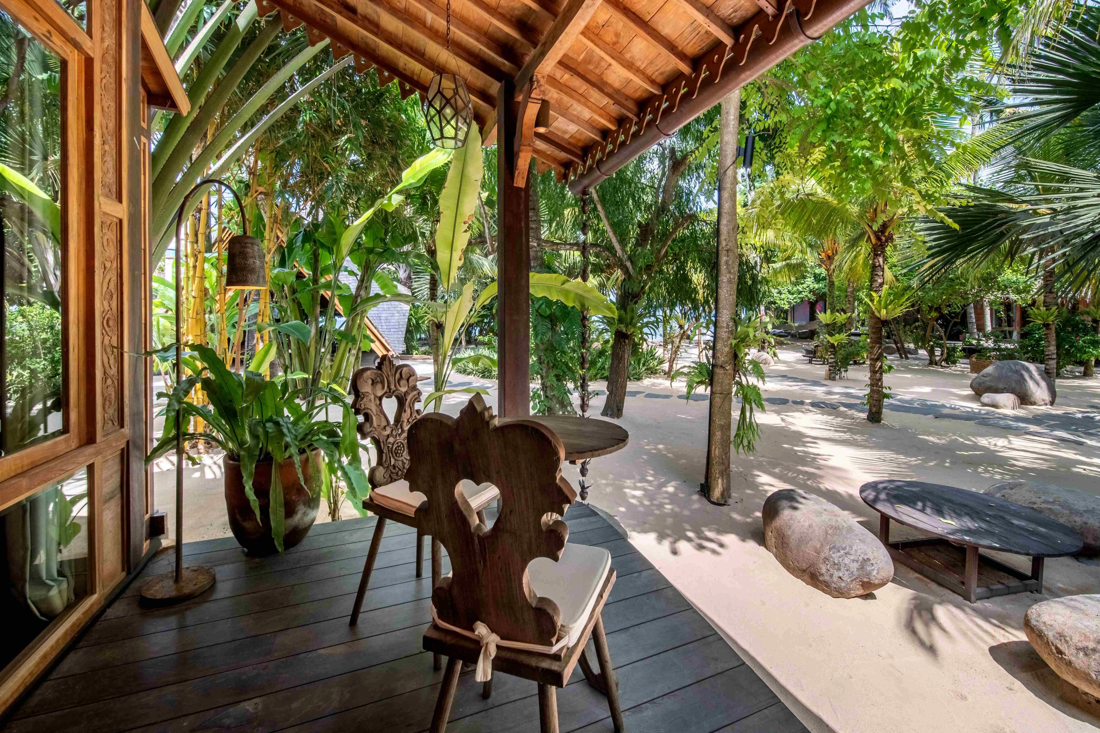 A carved timber chair on the villa's veranda, looking out across the sand courtyard.