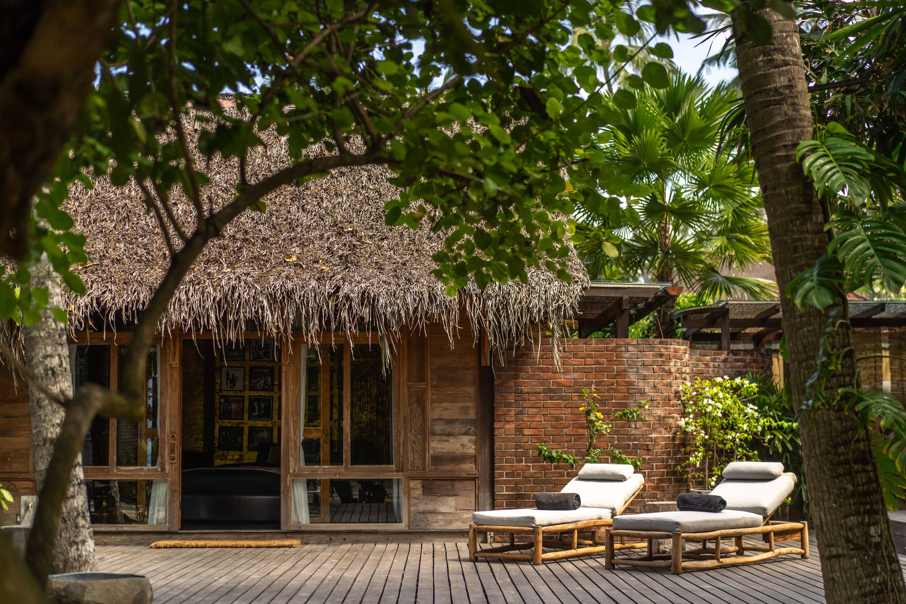 Two timber loungers on the deck outside the villa's thatched and brick façade.