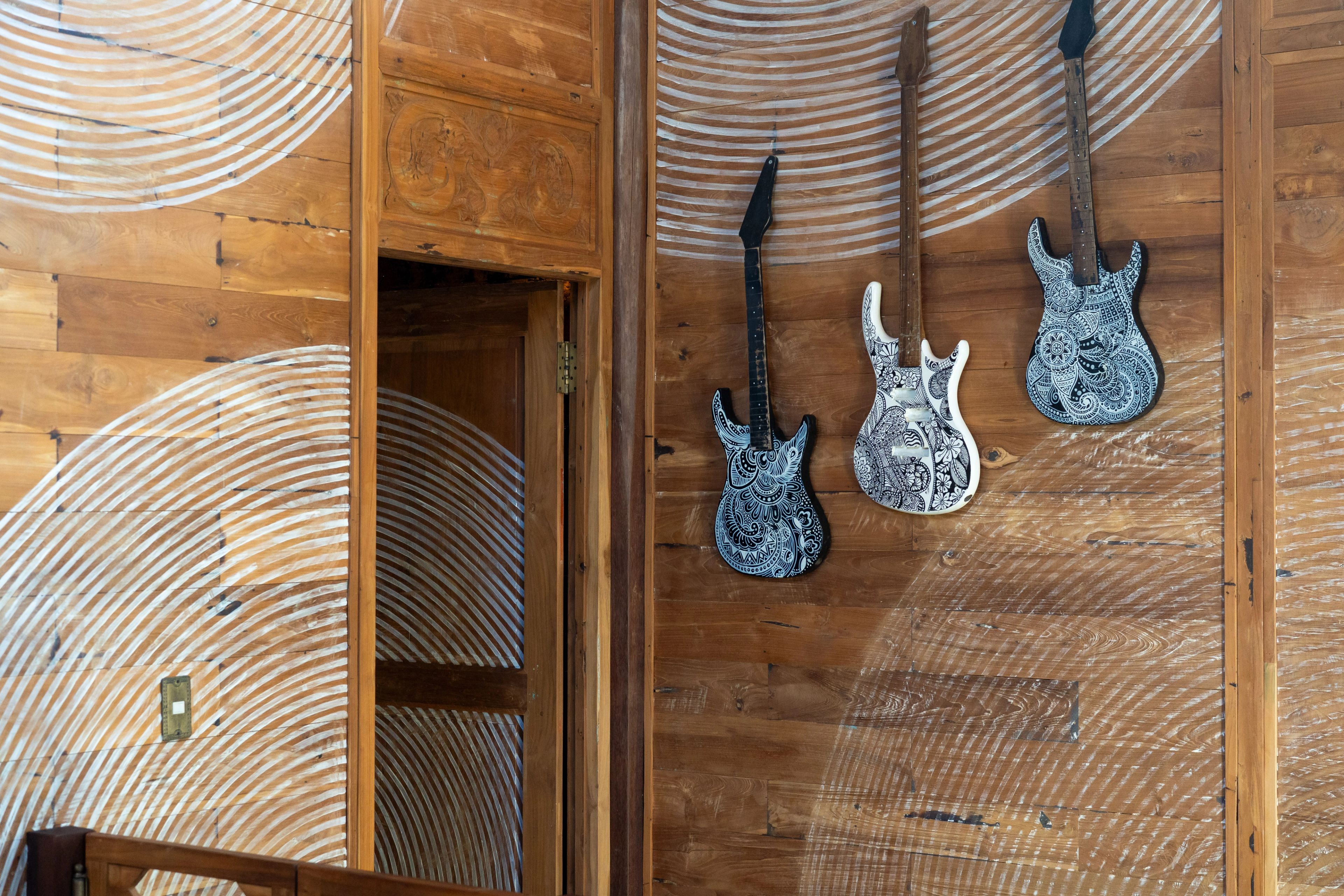 Three patterned electric guitars mounted on a timber wall beside a carved door.
