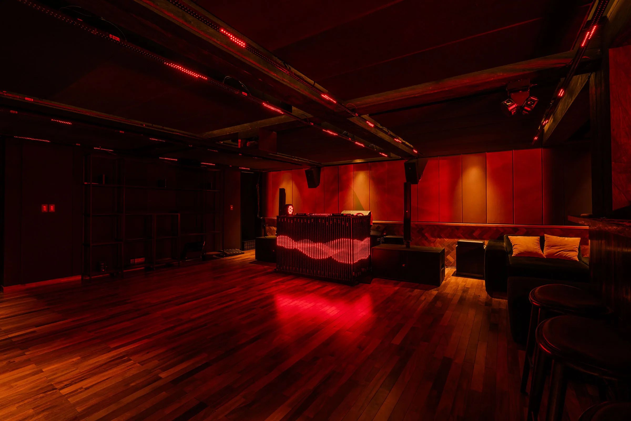 The empty basement club under red light, its timber floor running to booth seating at the far end.