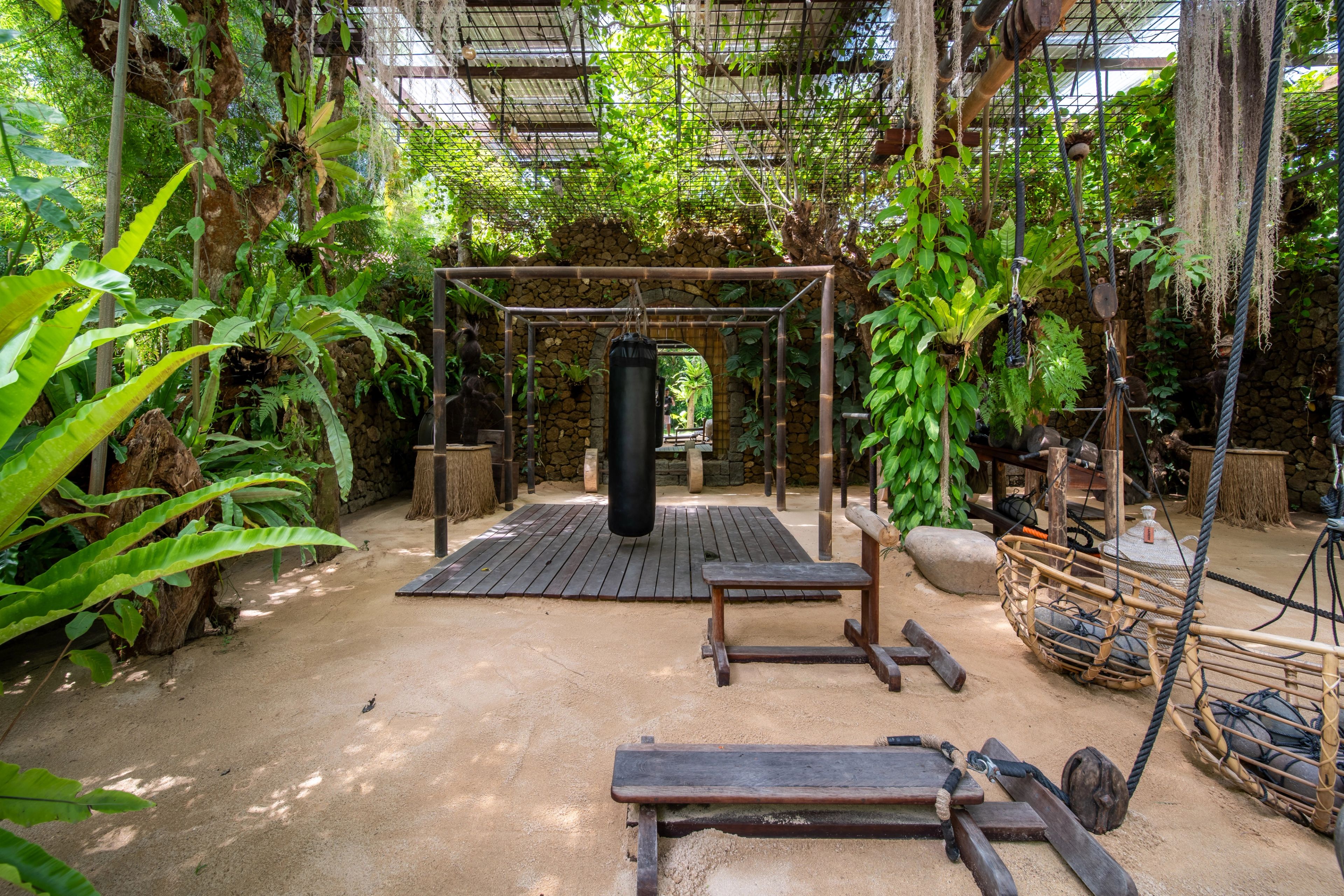 A punching bag hanging from the bamboo frame, with benches and the stone archway behind.