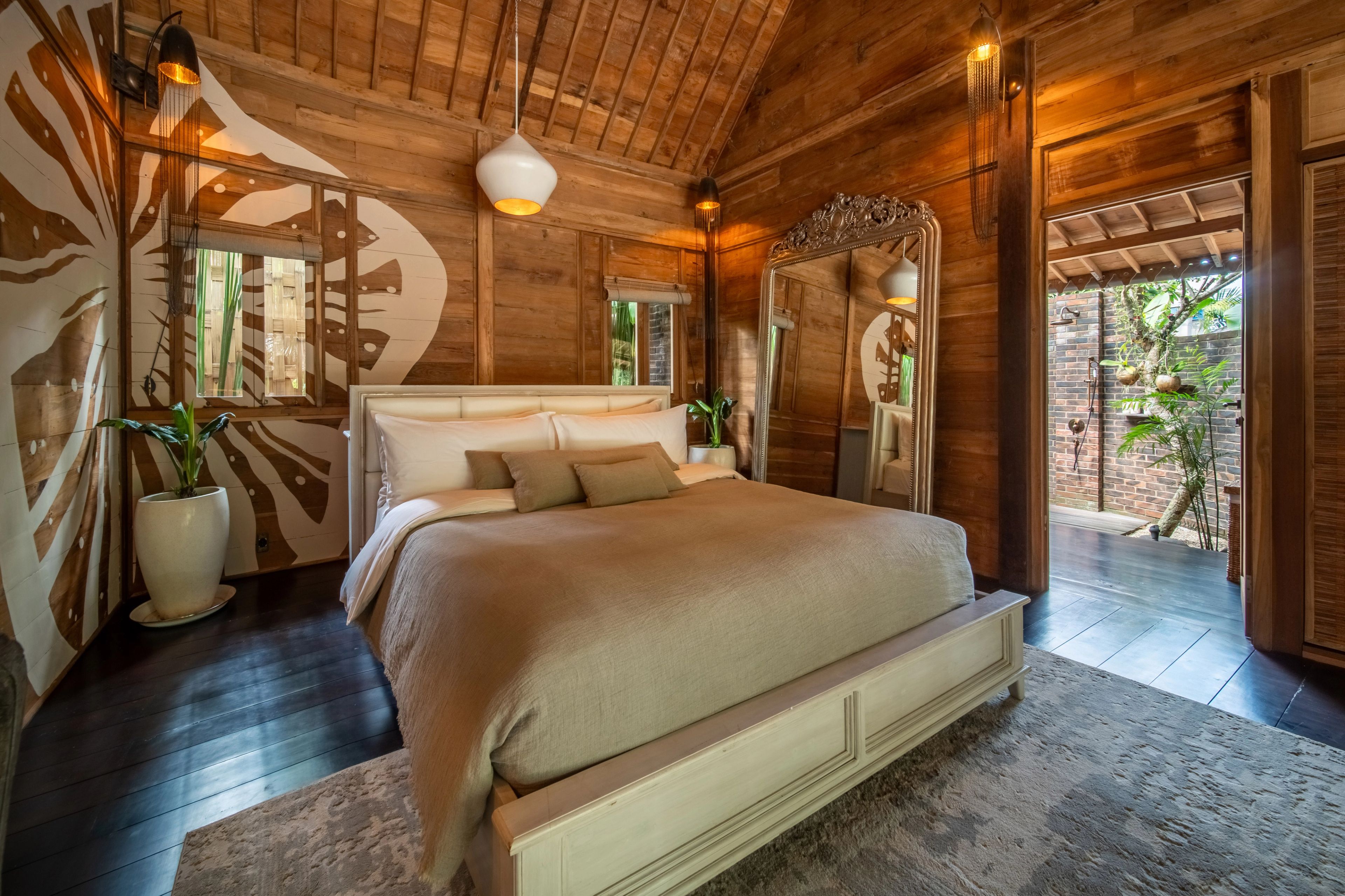 A made bed under a painted feature wall, mirrors alongside and doors open to the garden.