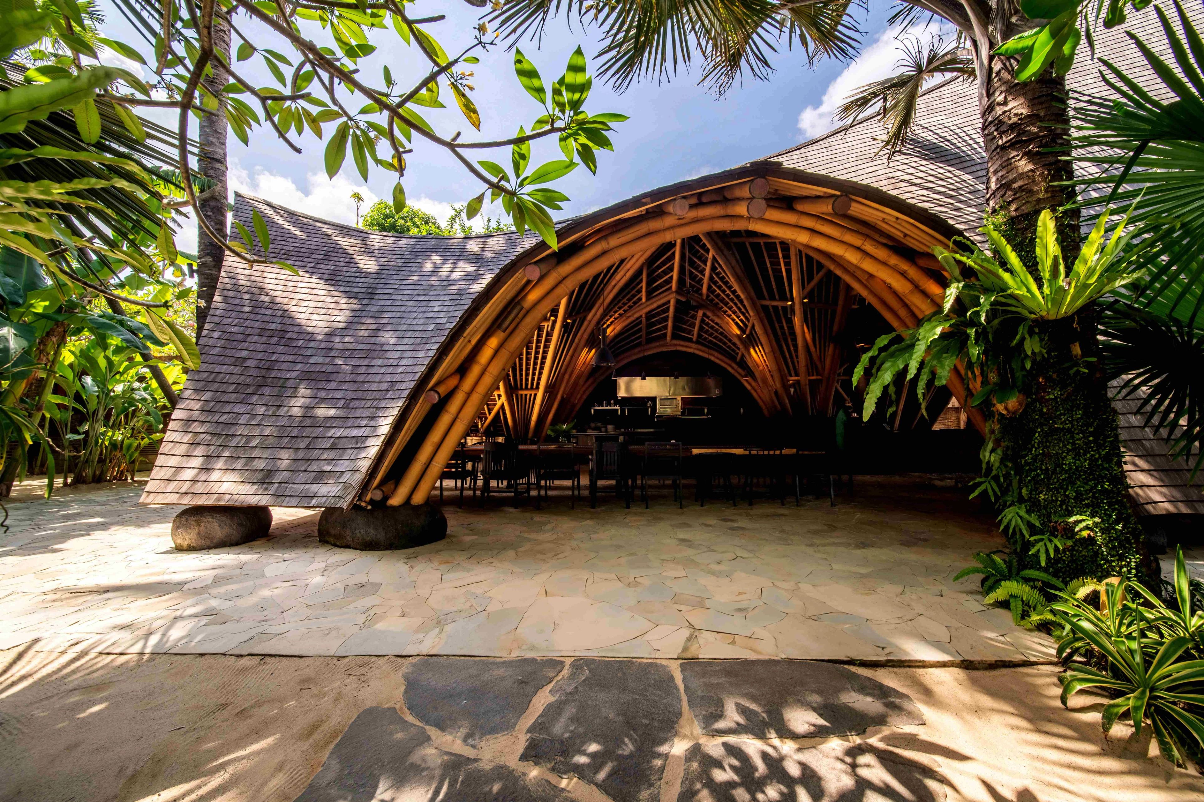 The curved bamboo shell of the restaurant seen from the flagstone path, open to the garden.