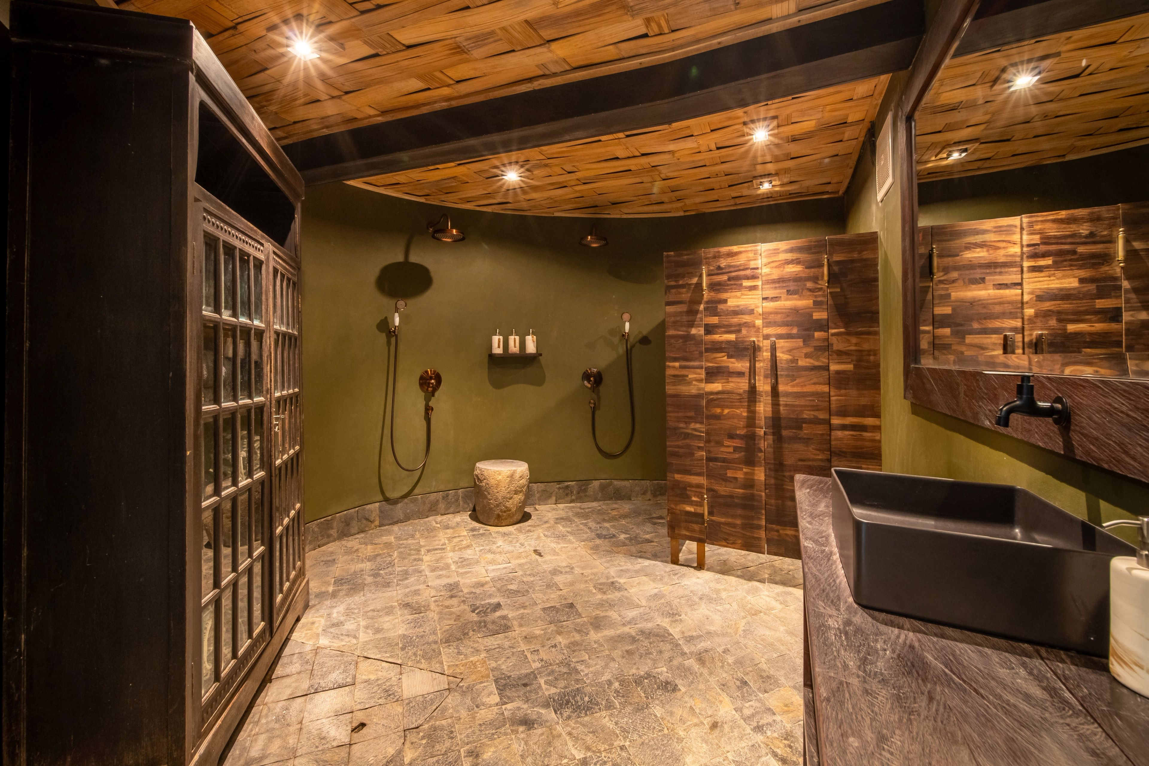 A stone shower room with twin rain heads, a timber stool and a deep basin under the panelled ceiling.