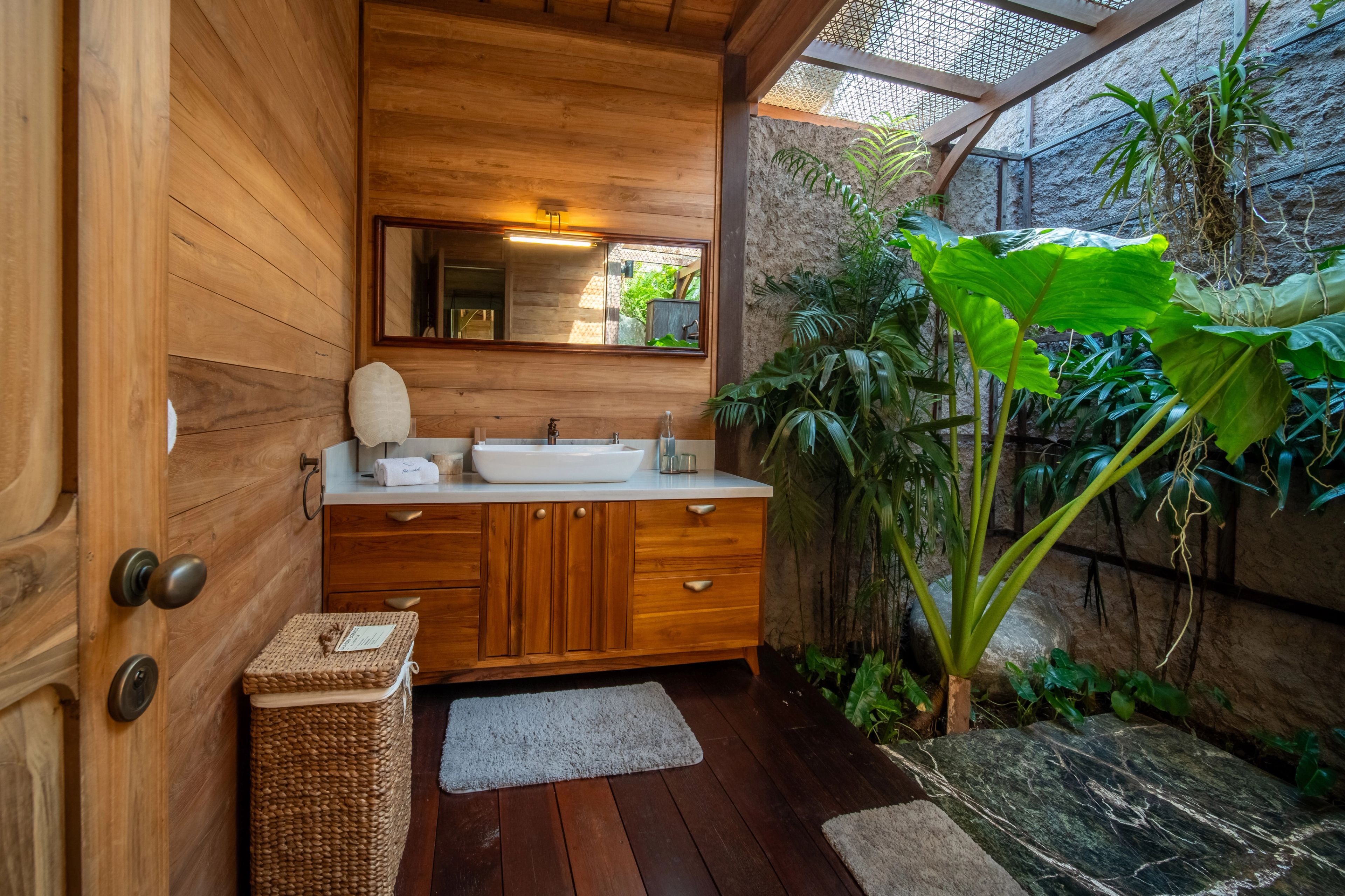 The bathroom vanity and mirror, the room open along one side to planting and a stone wall.