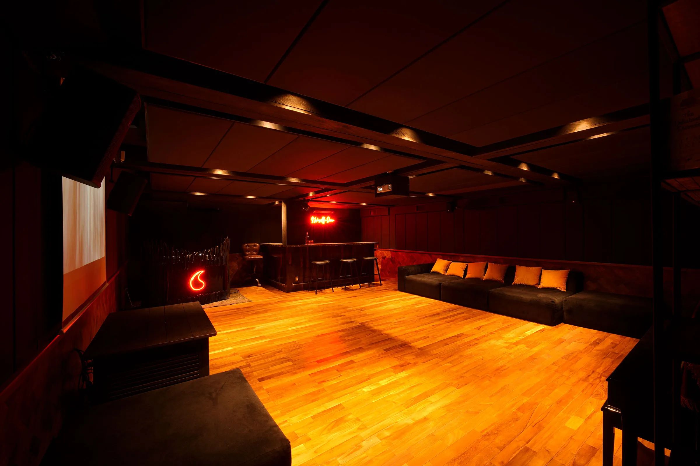 The basement club's parquet floor lit warm, banquette seating along the wall and neon at the far end.