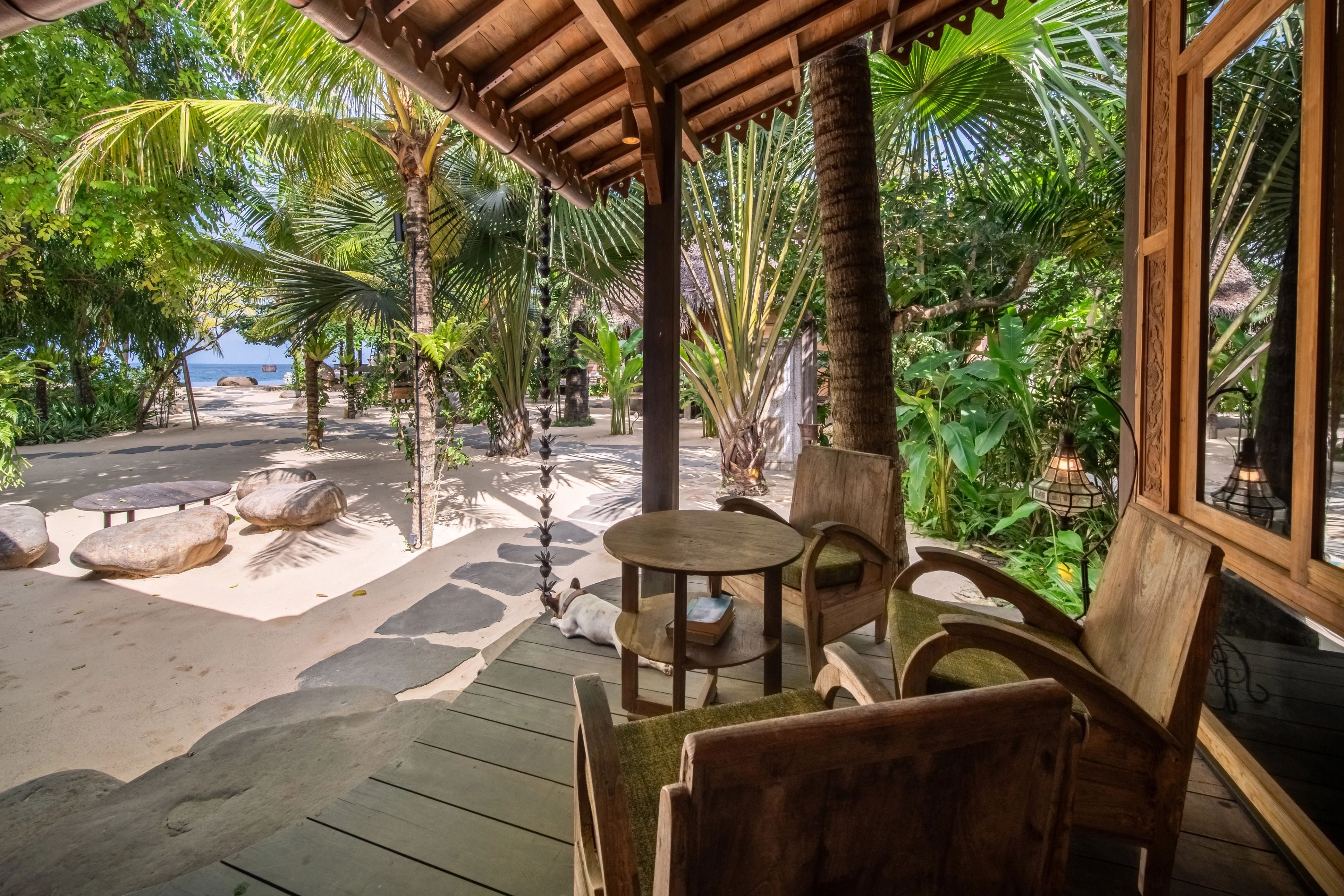 A timber armchair and side table on the veranda, the sand and palms running down to the sea.