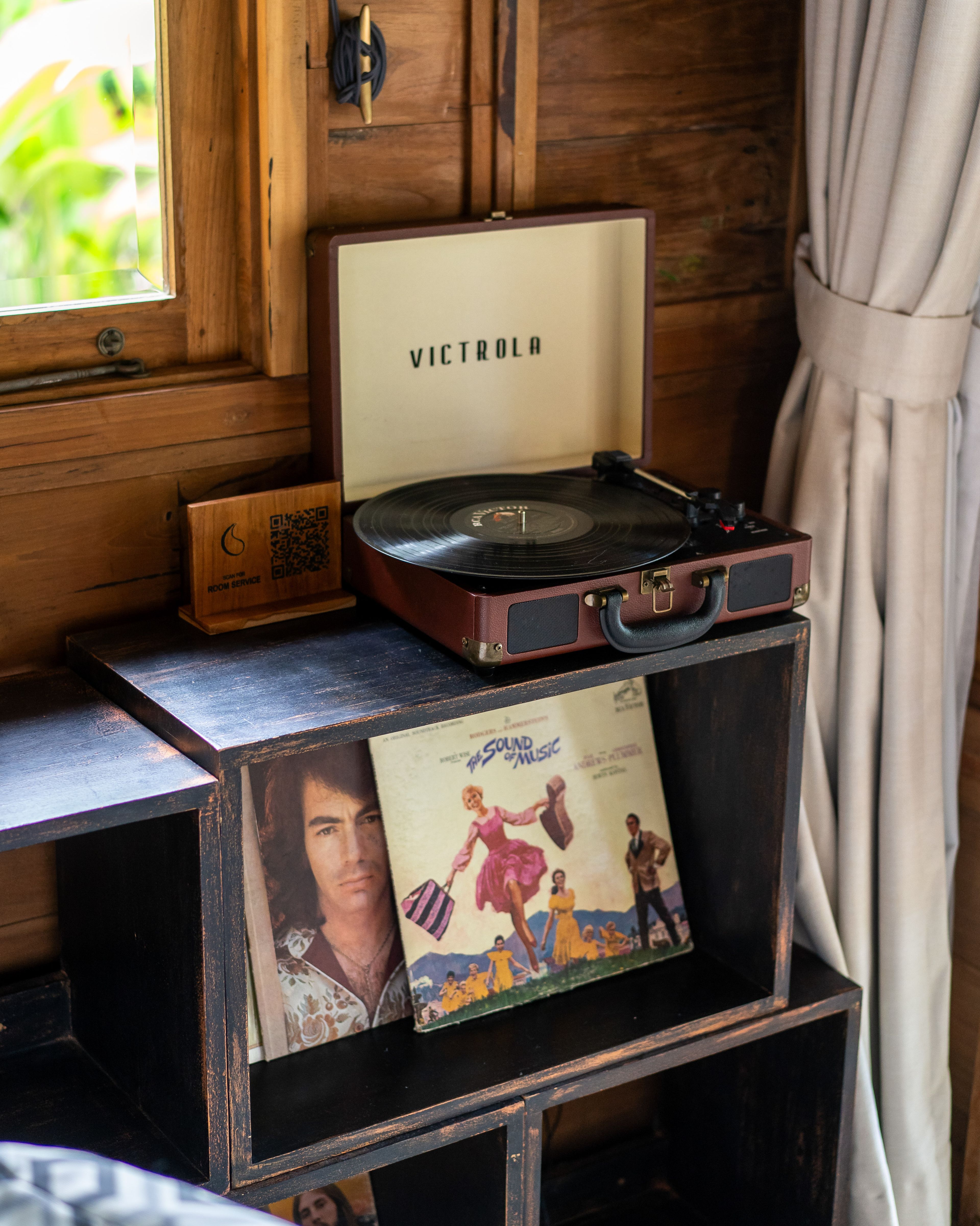 A portable turntable on a timber console with record sleeves propped below it.