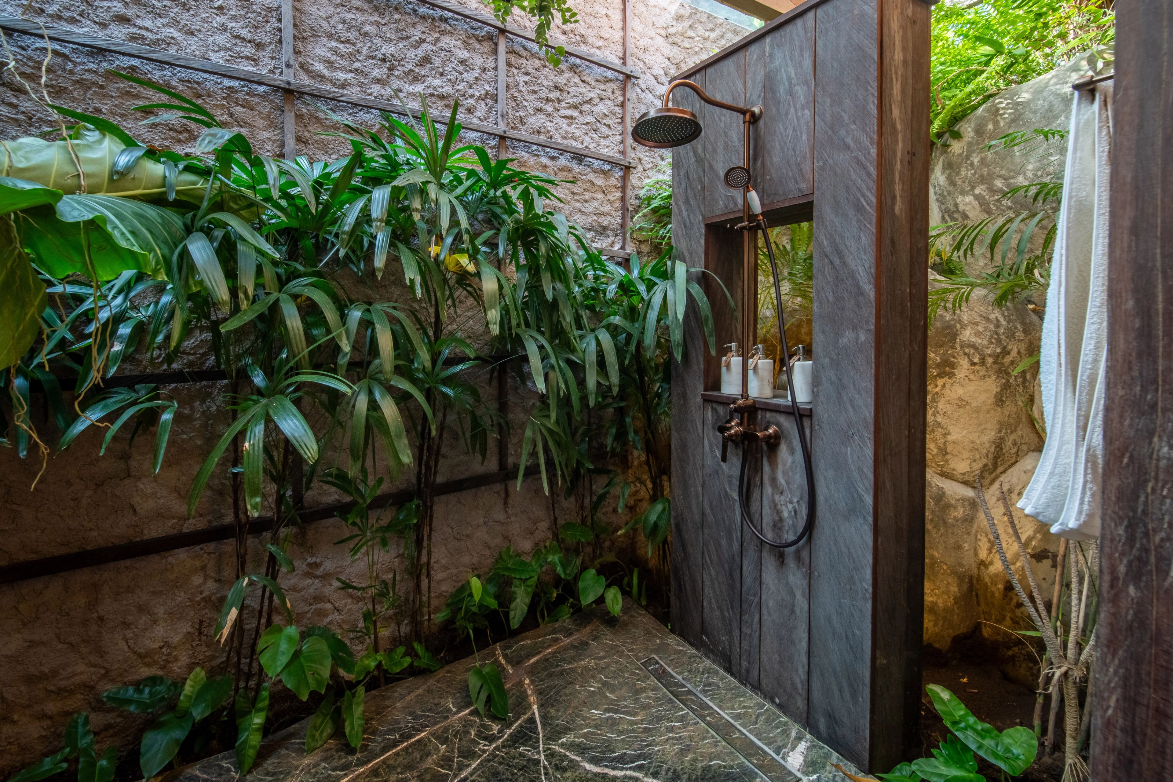 An outdoor shower set against a stone wall thick with planting, open to the sky.