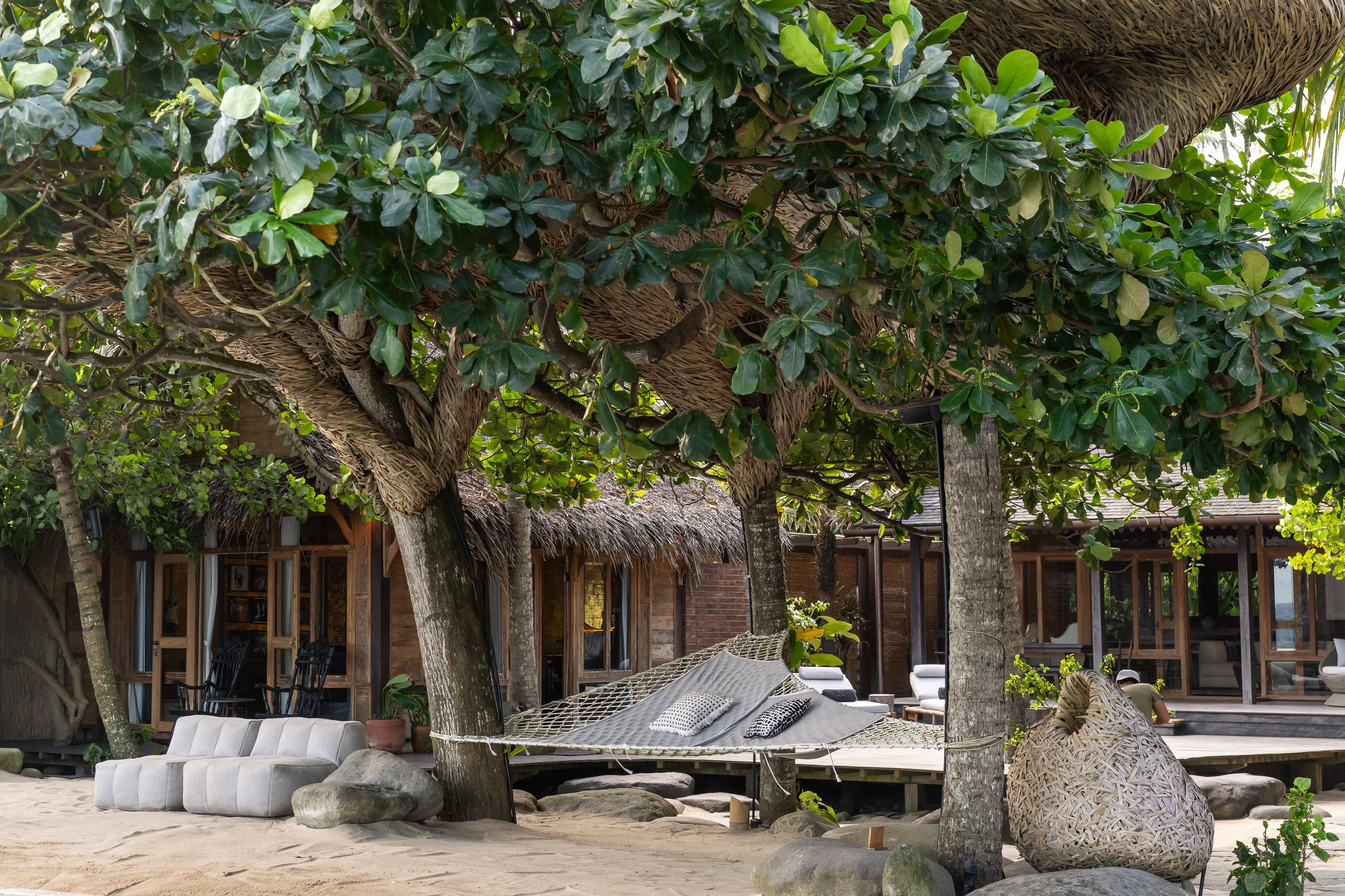 A hammock strung between trees over the sand courtyard, seating and villas around it.