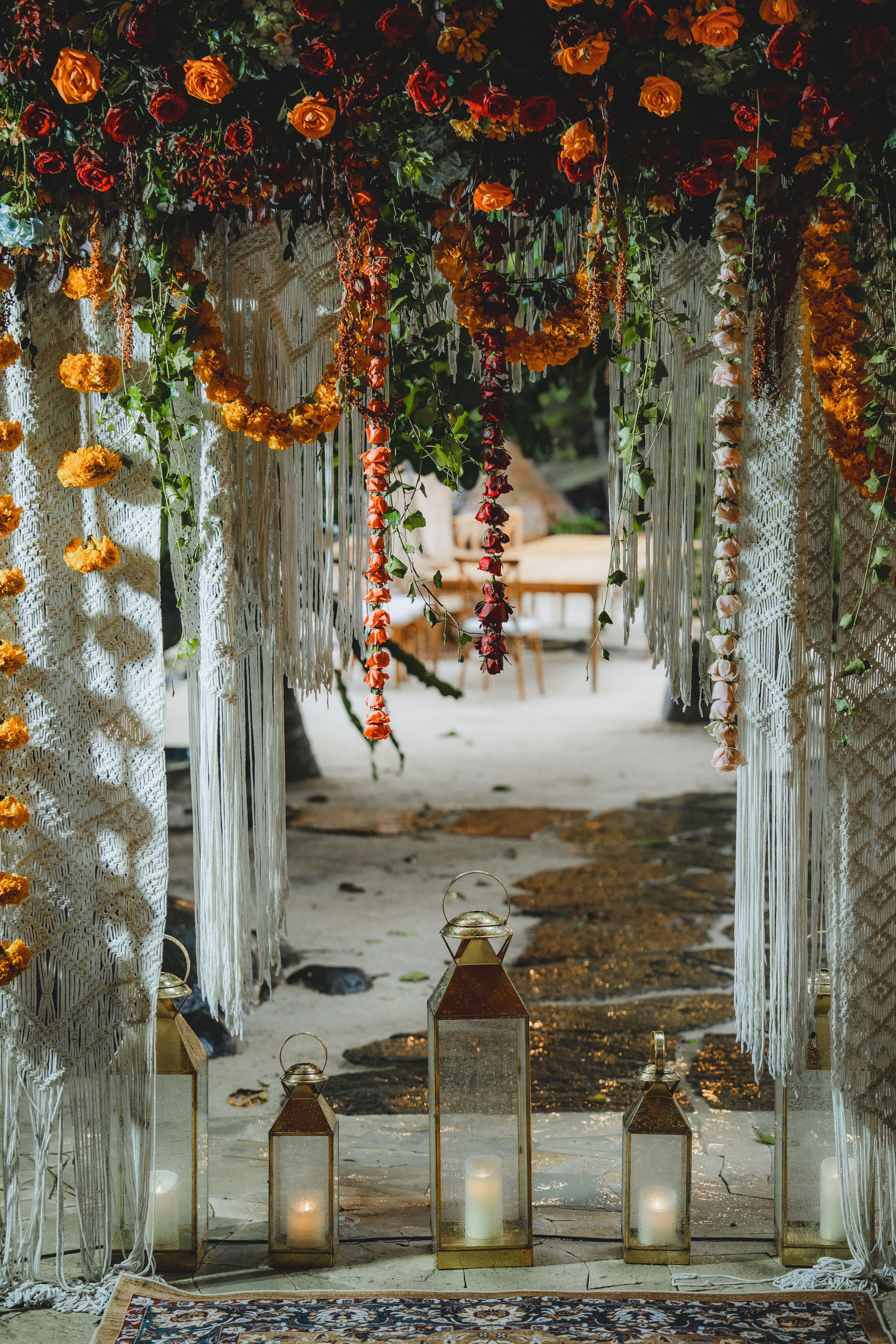 A macramé and flower-hung entrance framing the aisle, marigold strands falling either side.