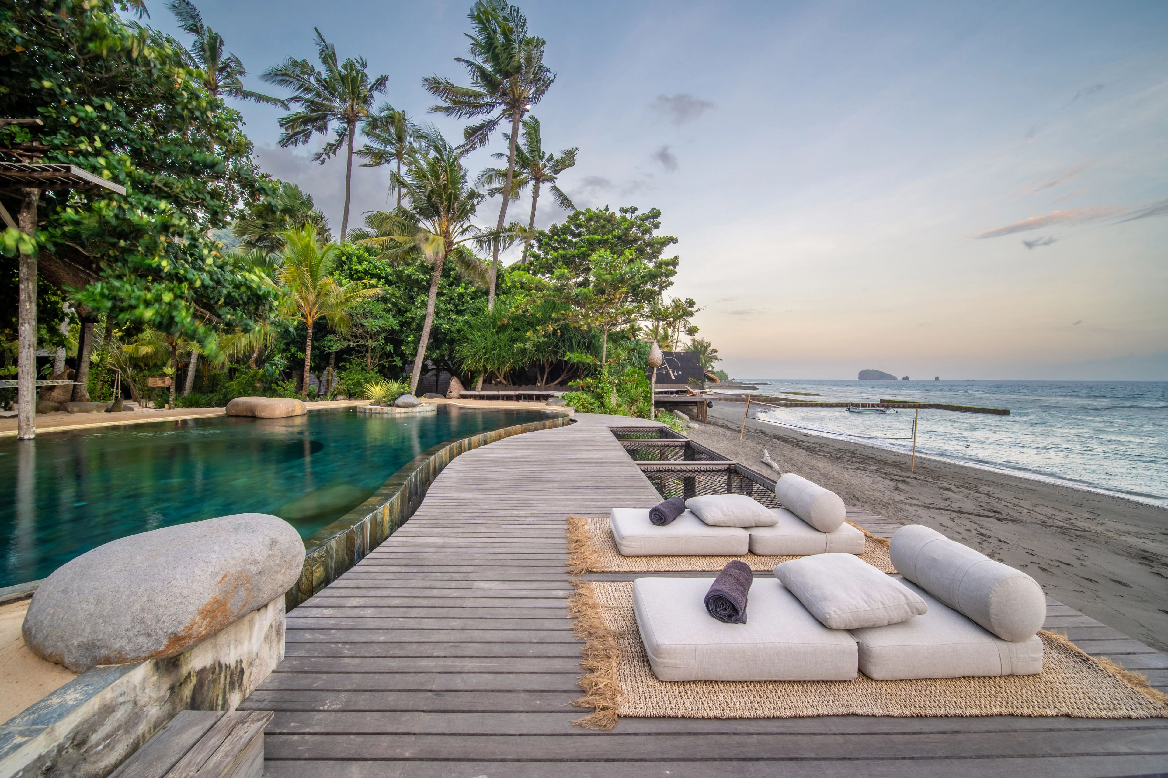Daybeds laid out on the deck between the pool and the beach in soft morning light.