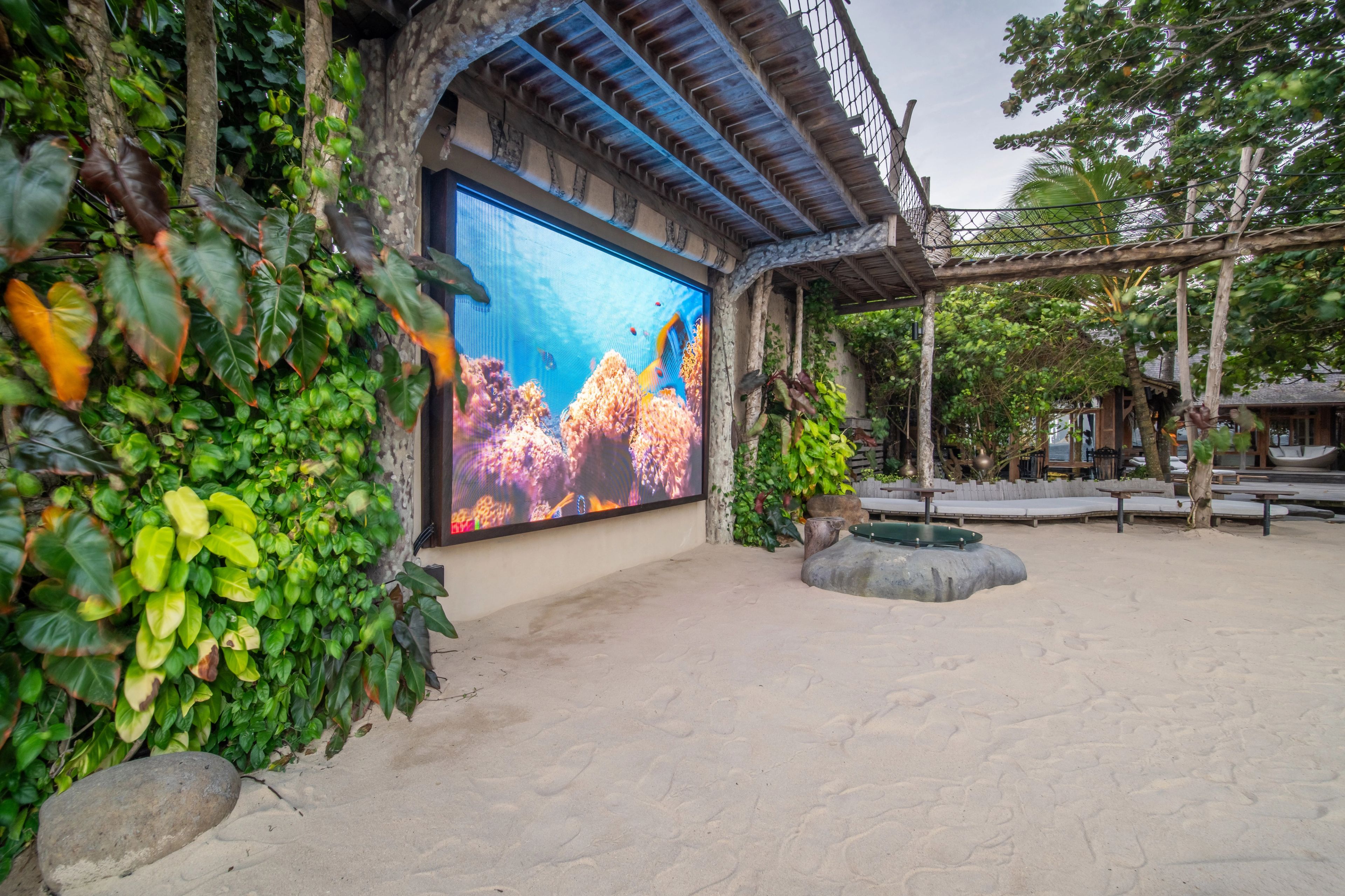 Outdoor cinema screen displaying underwater coral reef footage framed by lush greenery at The Seed Bali.