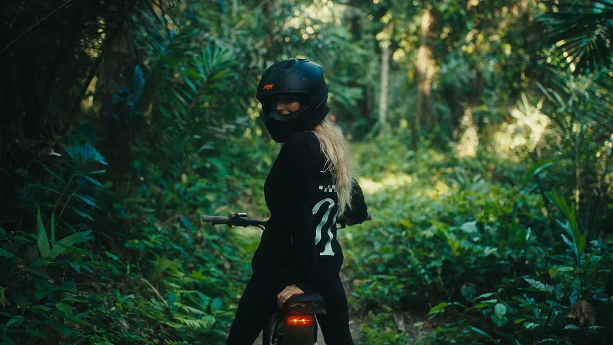 A helmeted rider on an electric bike on a narrow track through dense jungle.