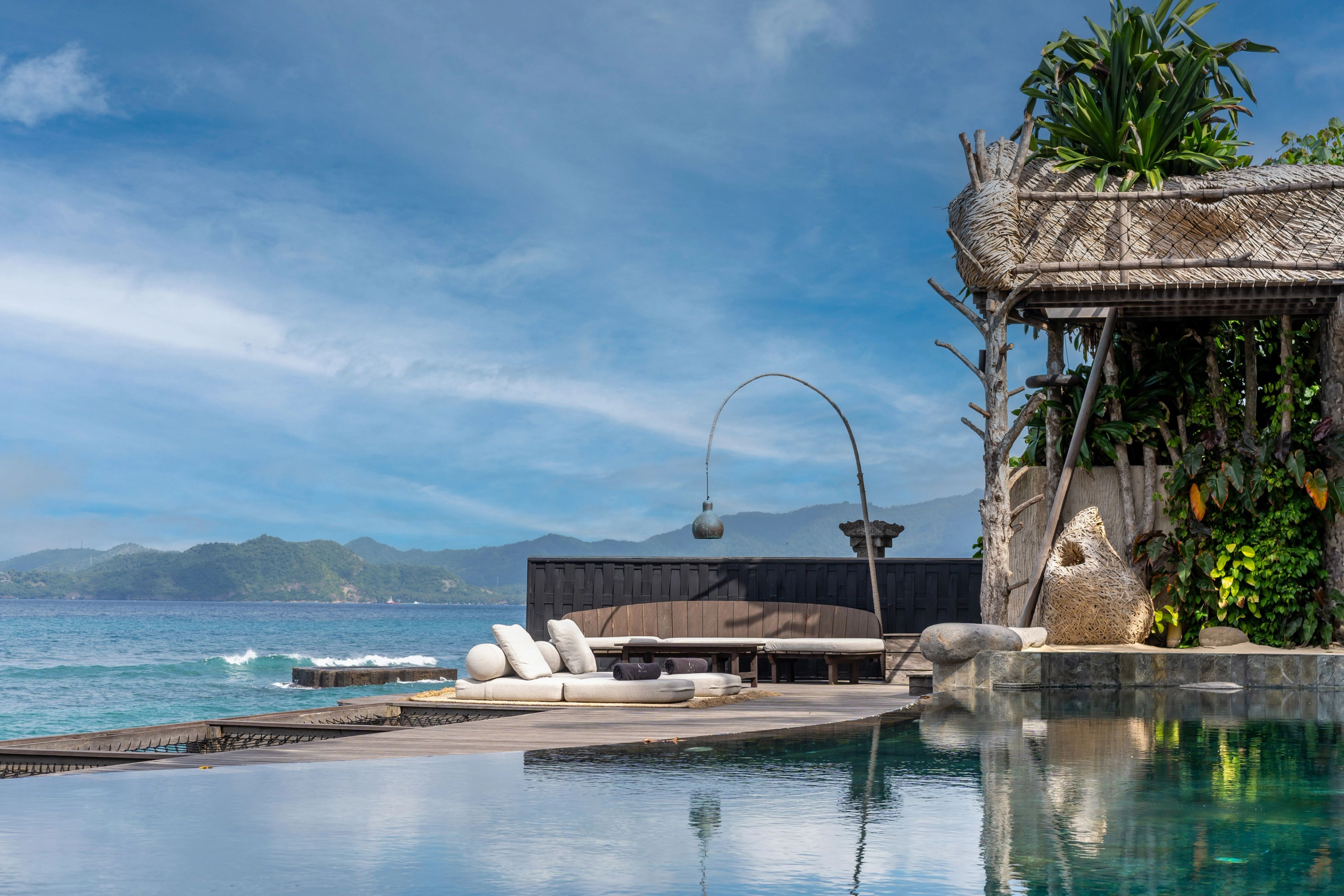 Daybeds and the thatched pavilion mirrored in the still surface of the infinity pool.
