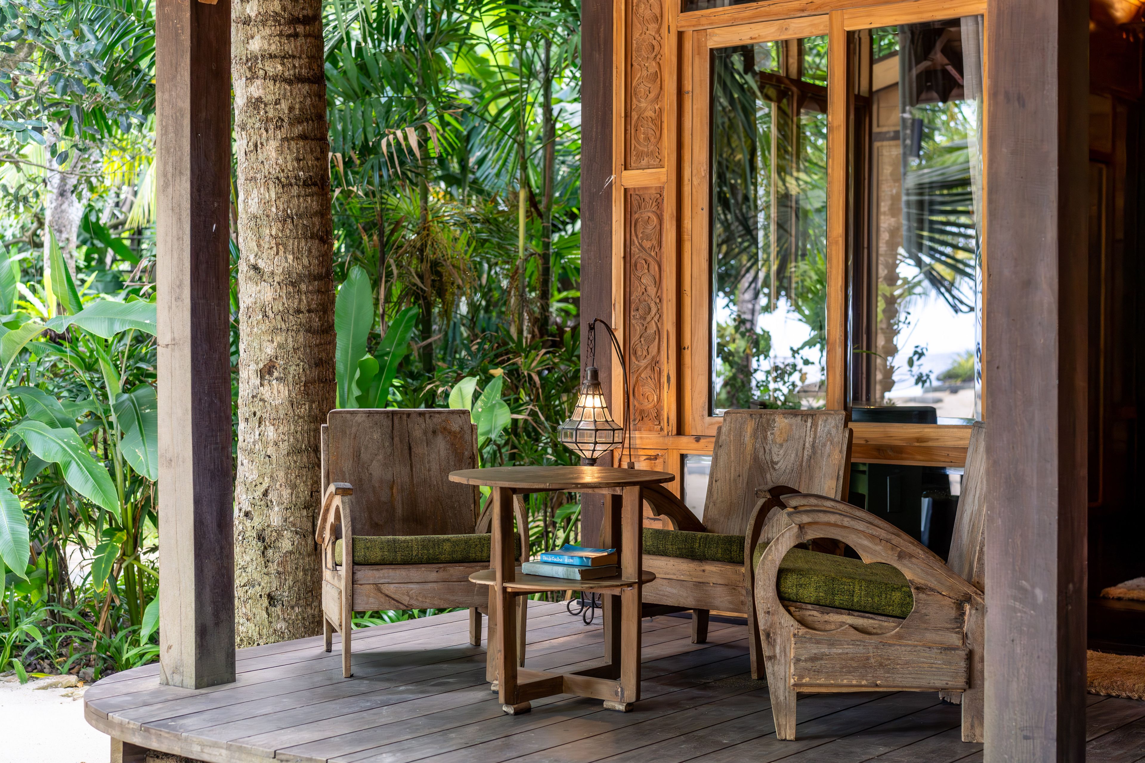 Two timber armchairs and a side table on the veranda between the posts, garden all around.