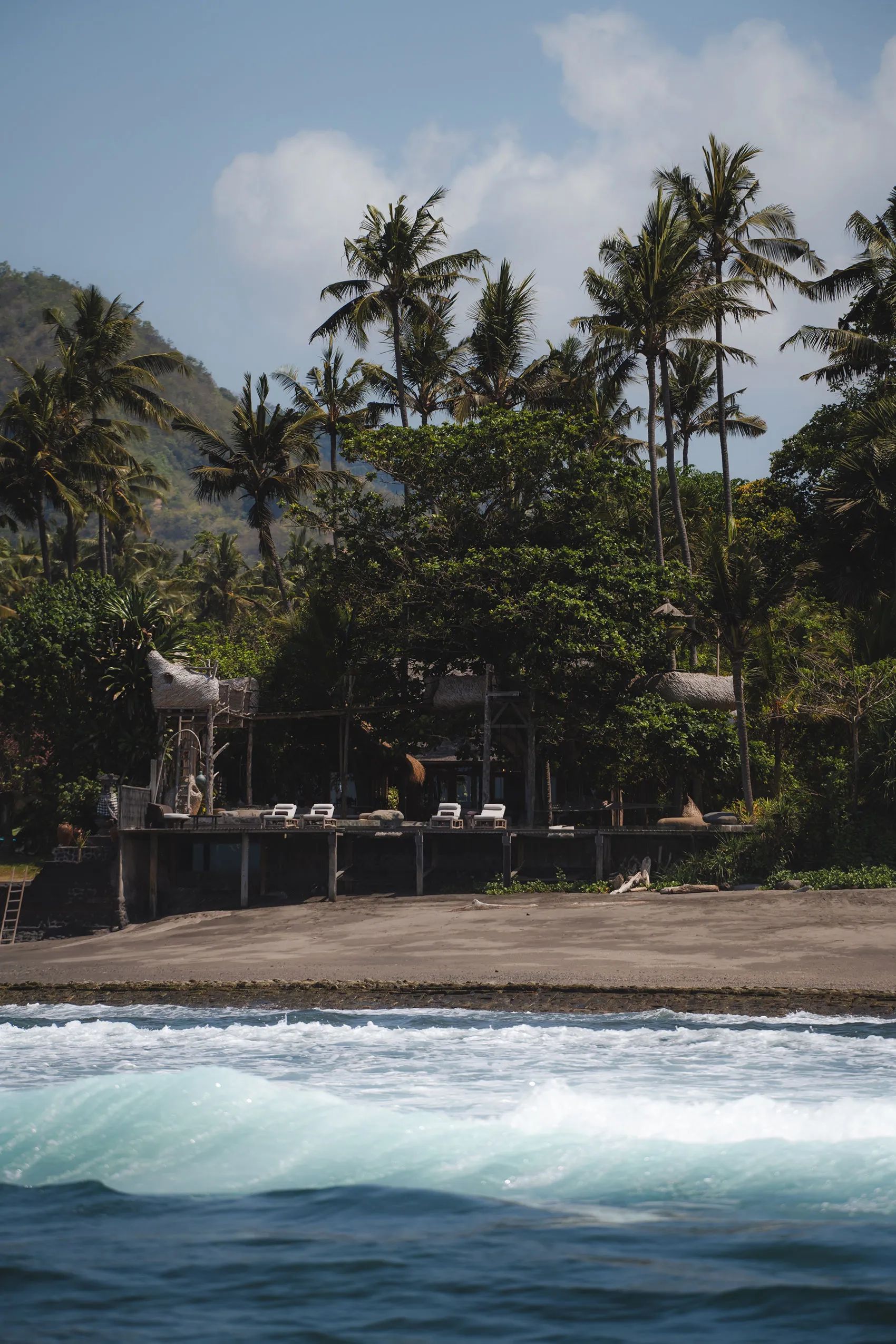 The property seen from the sand at dusk, loungers along the pool terrace under the palms.
