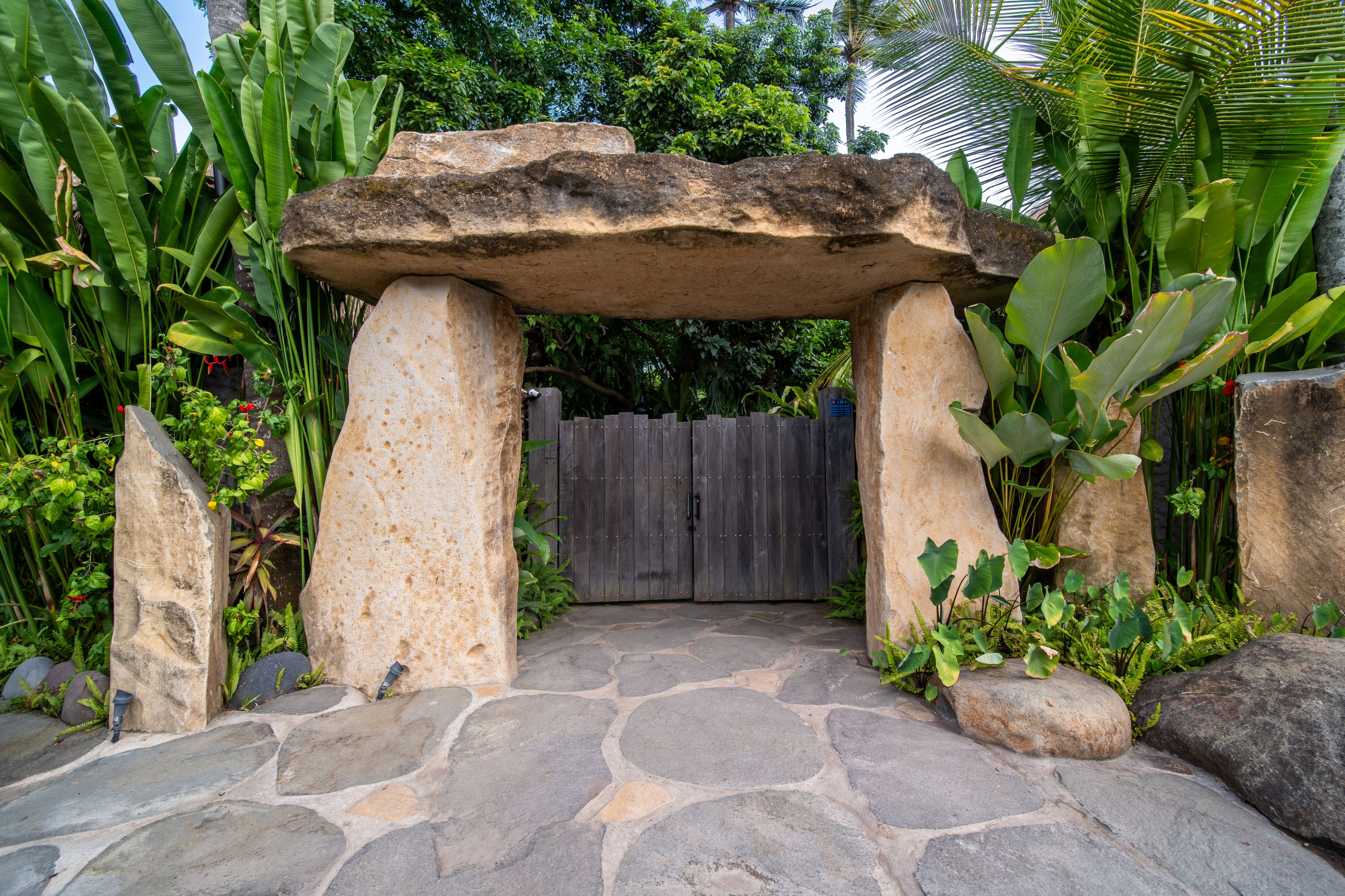 A megalithic stone gateway with a timber gate beneath it, set on a flagstone terrace among the planting.