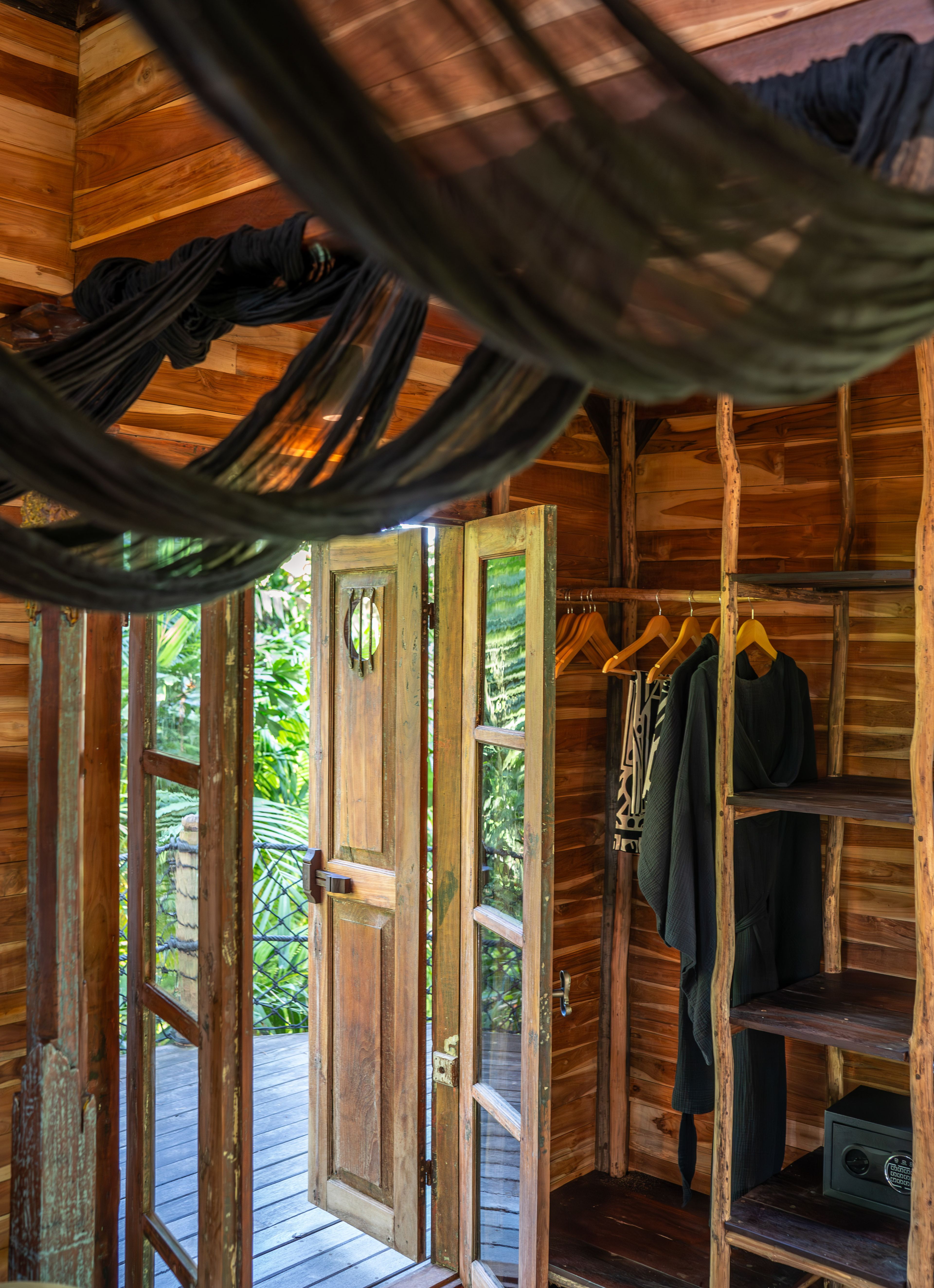 Robes hanging on a rail in the open wardrobe, beside doors opening to the trees.