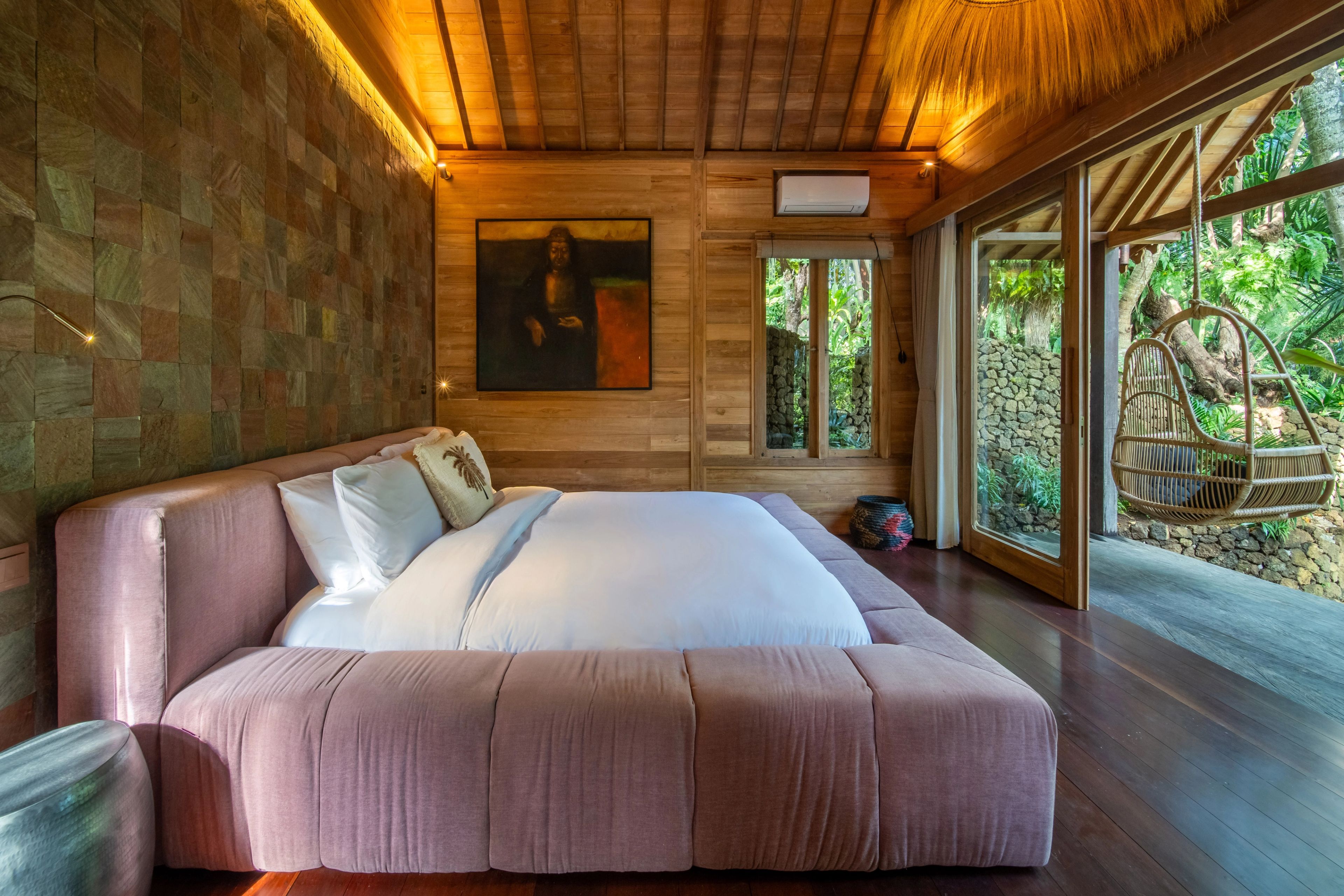 The bed made up in white against a tiled wall, doors open to the hanging chair on the deck.