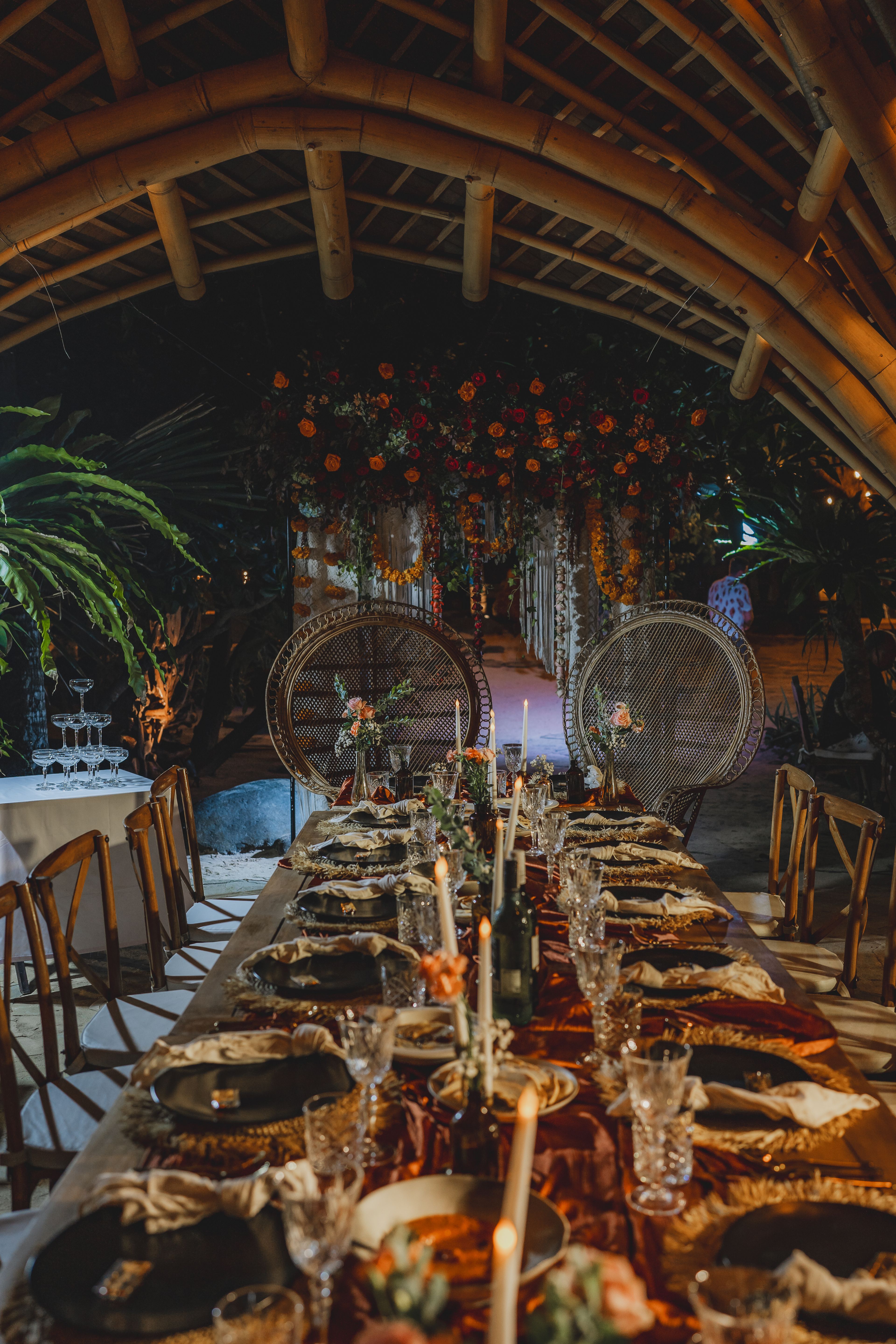A long white banquet table under tall tapers and low white arrangements, set on the lawn at dusk.