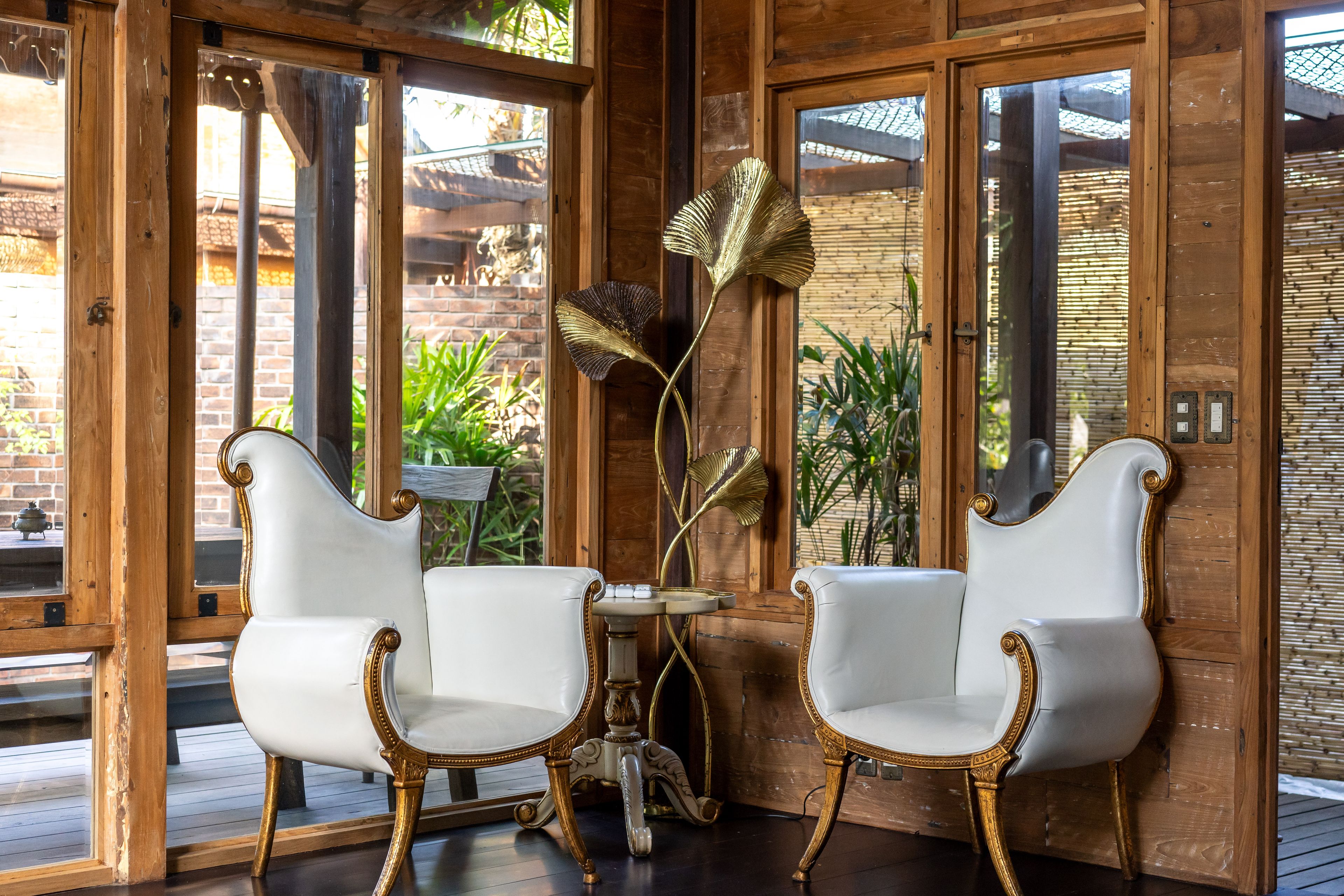 A pair of white armchairs either side of a small table, windows onto the garden behind.