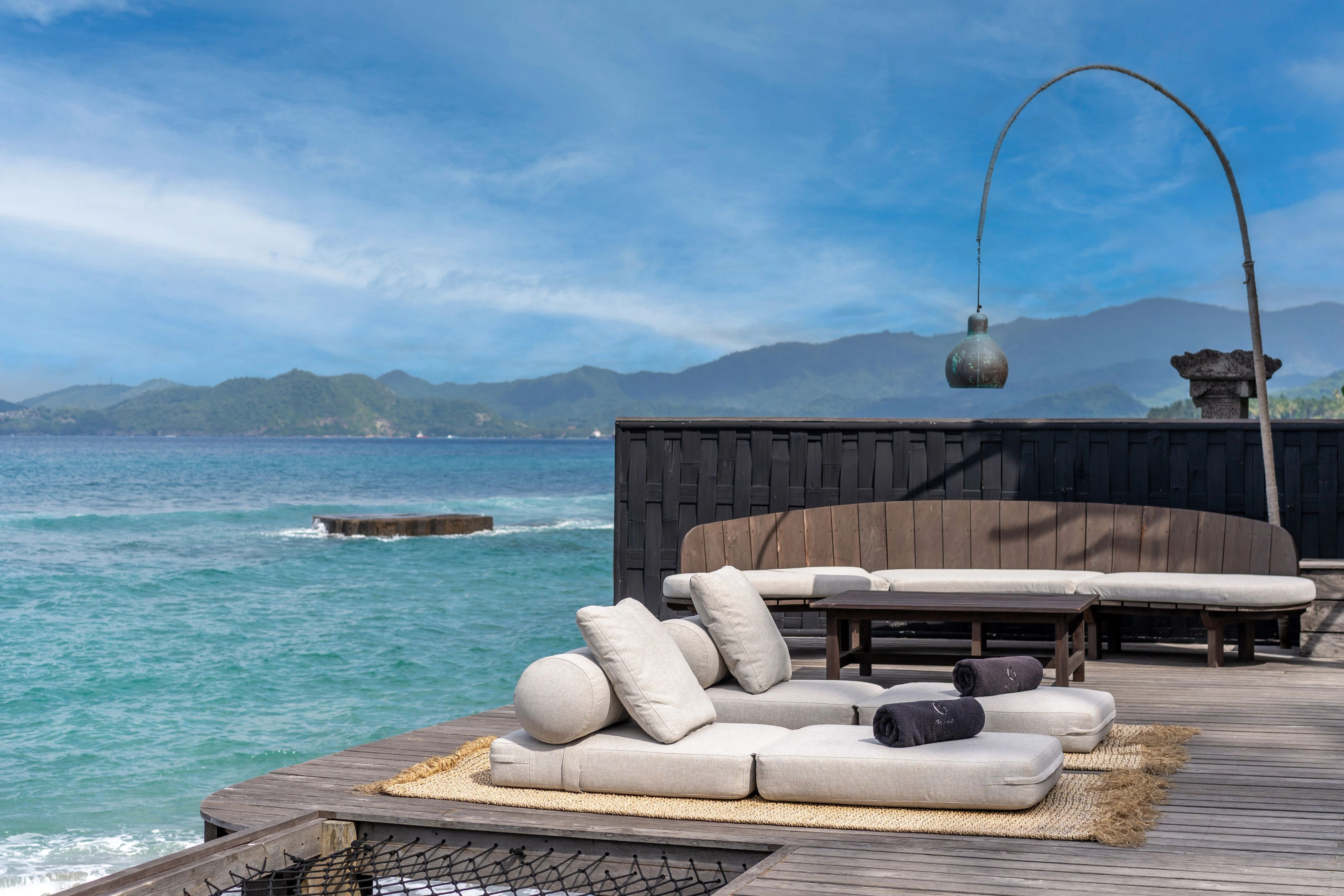 Daybeds and a bench under an arched lamp on the timber deck, looking out to the headland.
