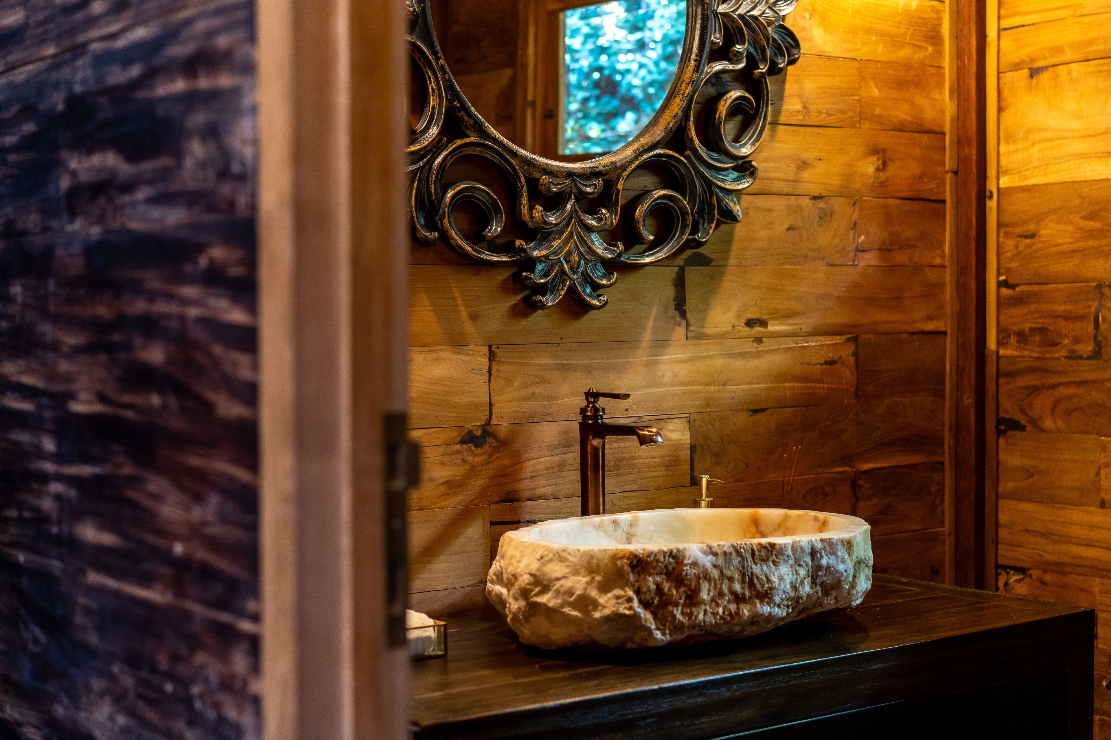A stone basin on a timber counter below an ornately carved mirror.