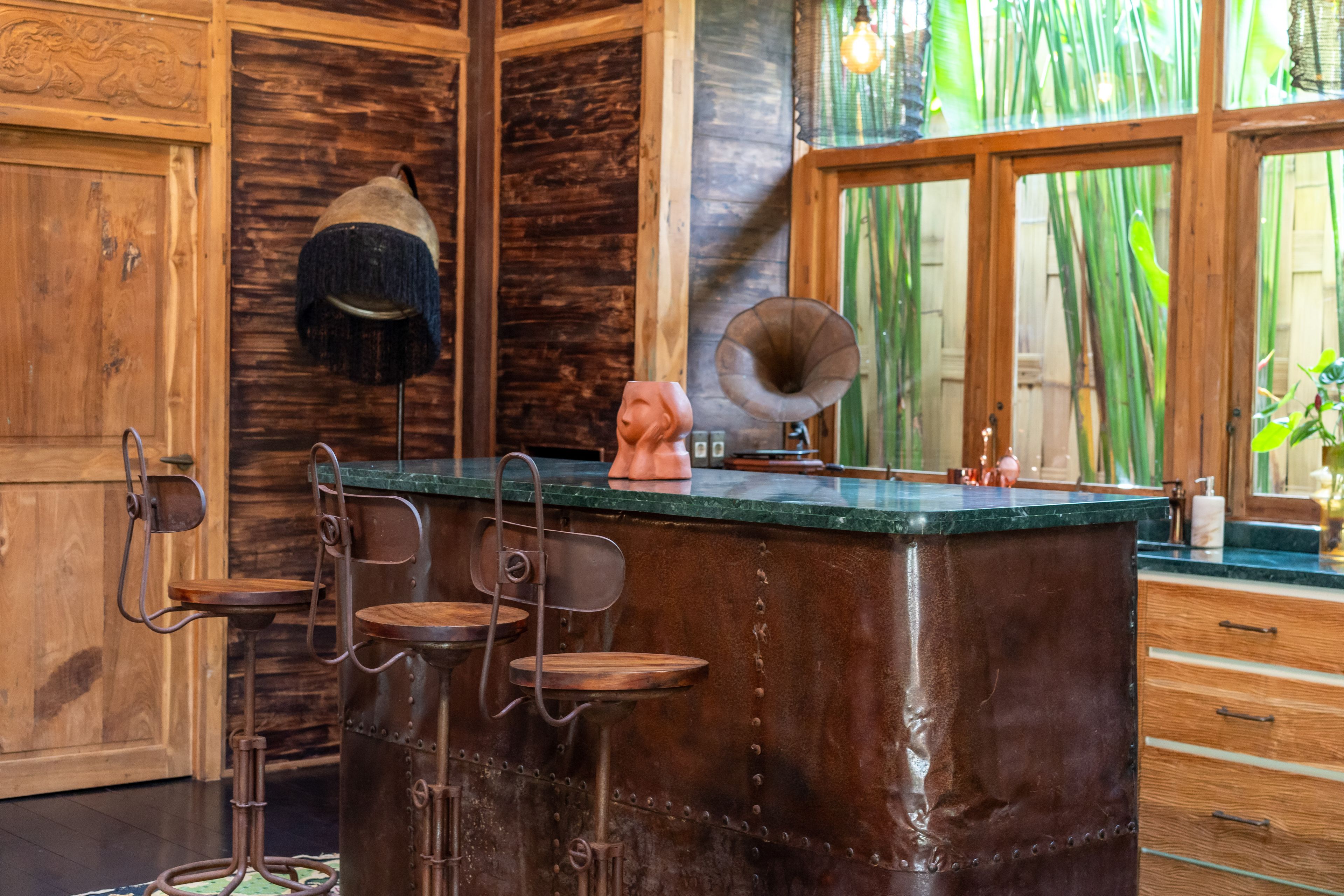 Metal stools at the green stone bar, gramophone and hat on the counter, bamboo through the windows.