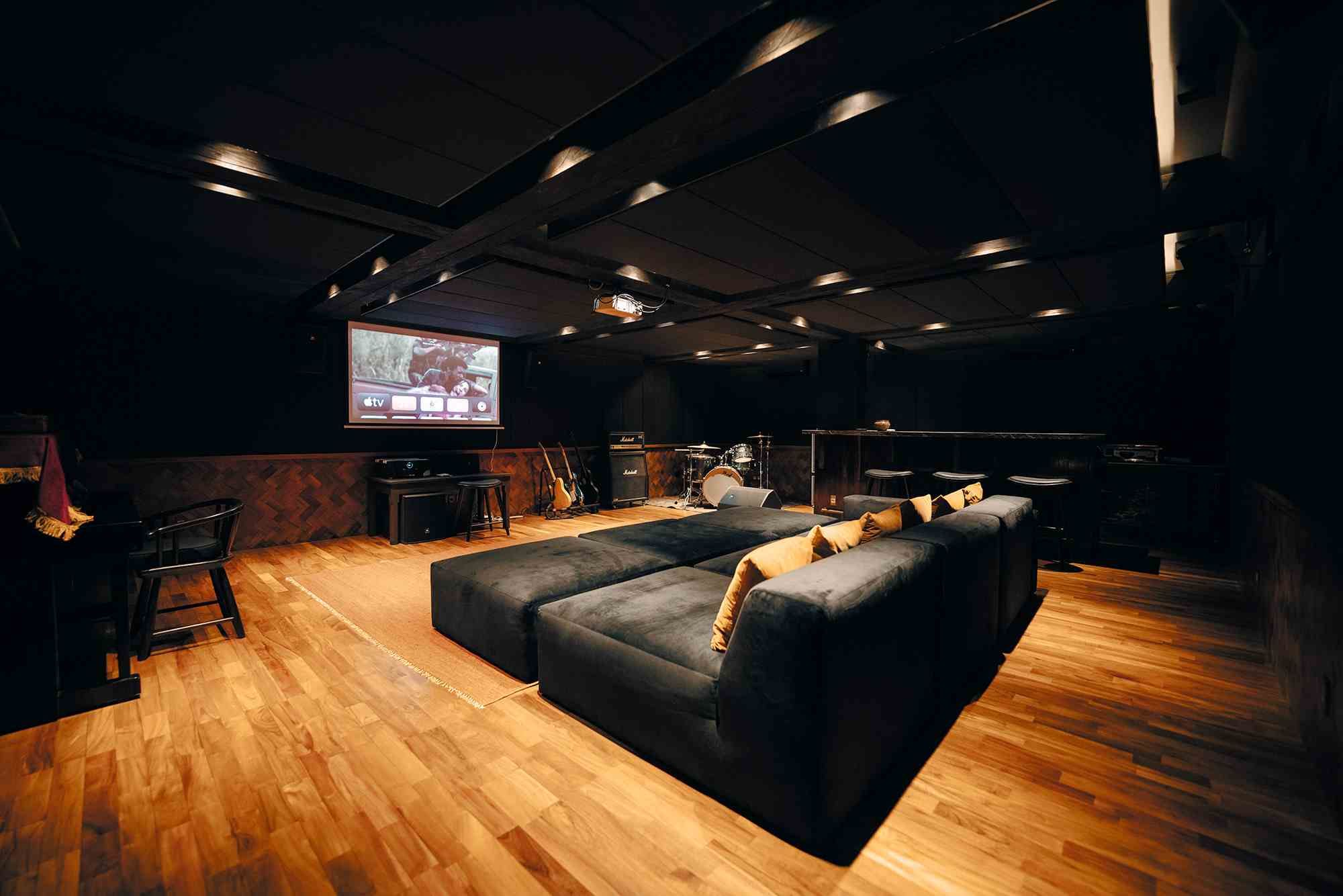 Deep modular sofas facing the projector screen in the basement, under a dark coffered ceiling.