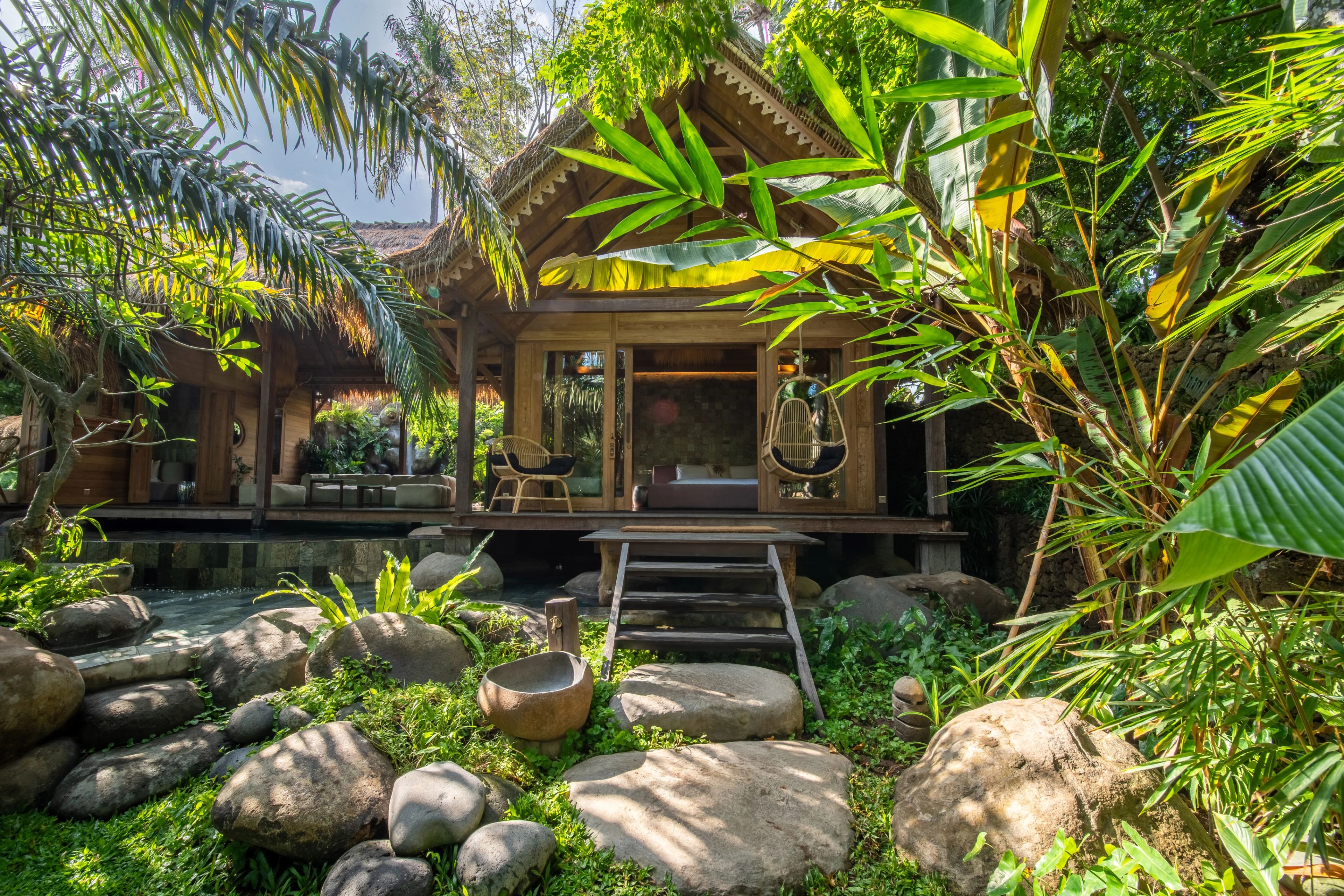 The villa across the boulders and grass of the garden, a hanging chair on its deck.