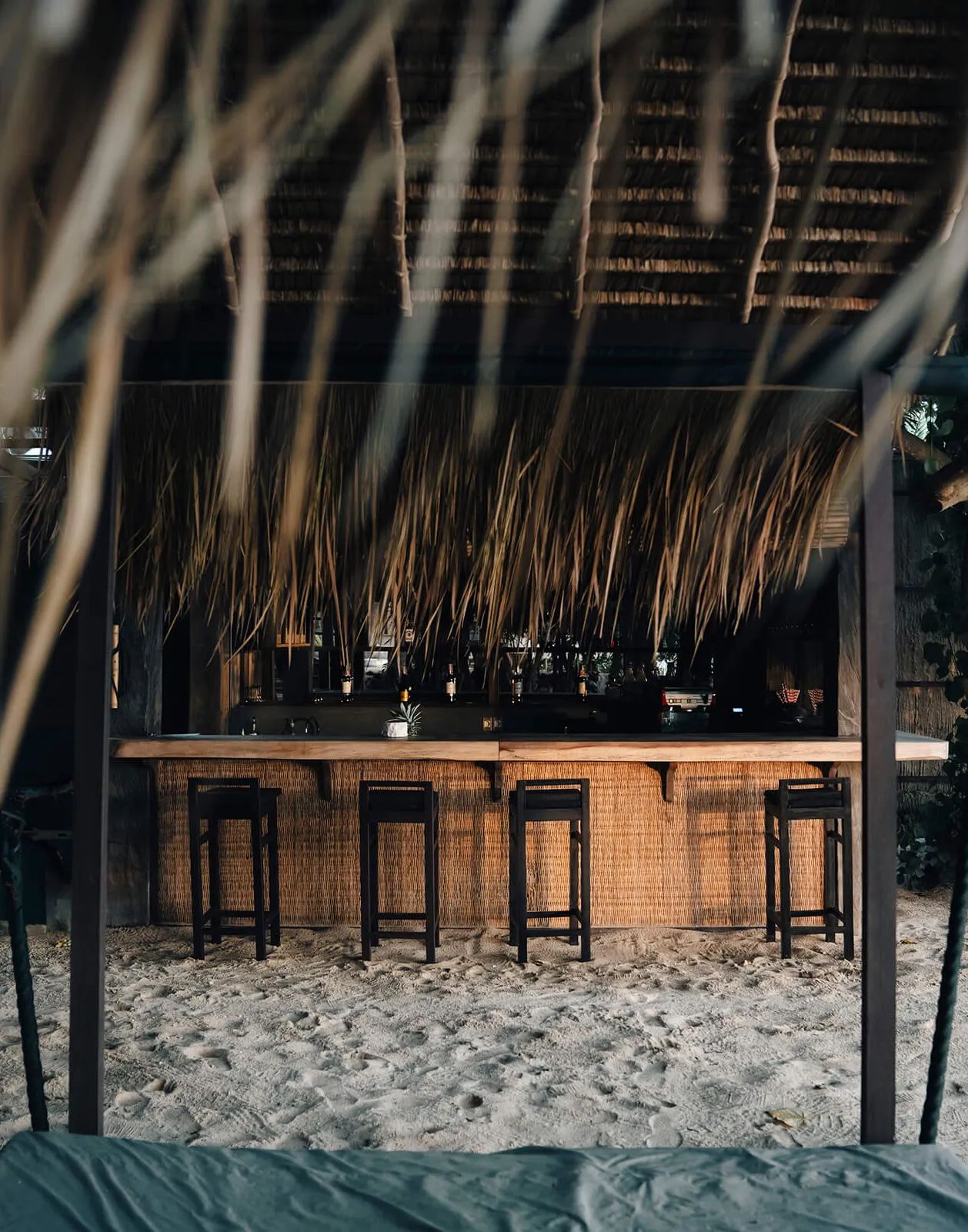 Stools drawn up to a thatched beach bar, bottles ranged along the back counter.