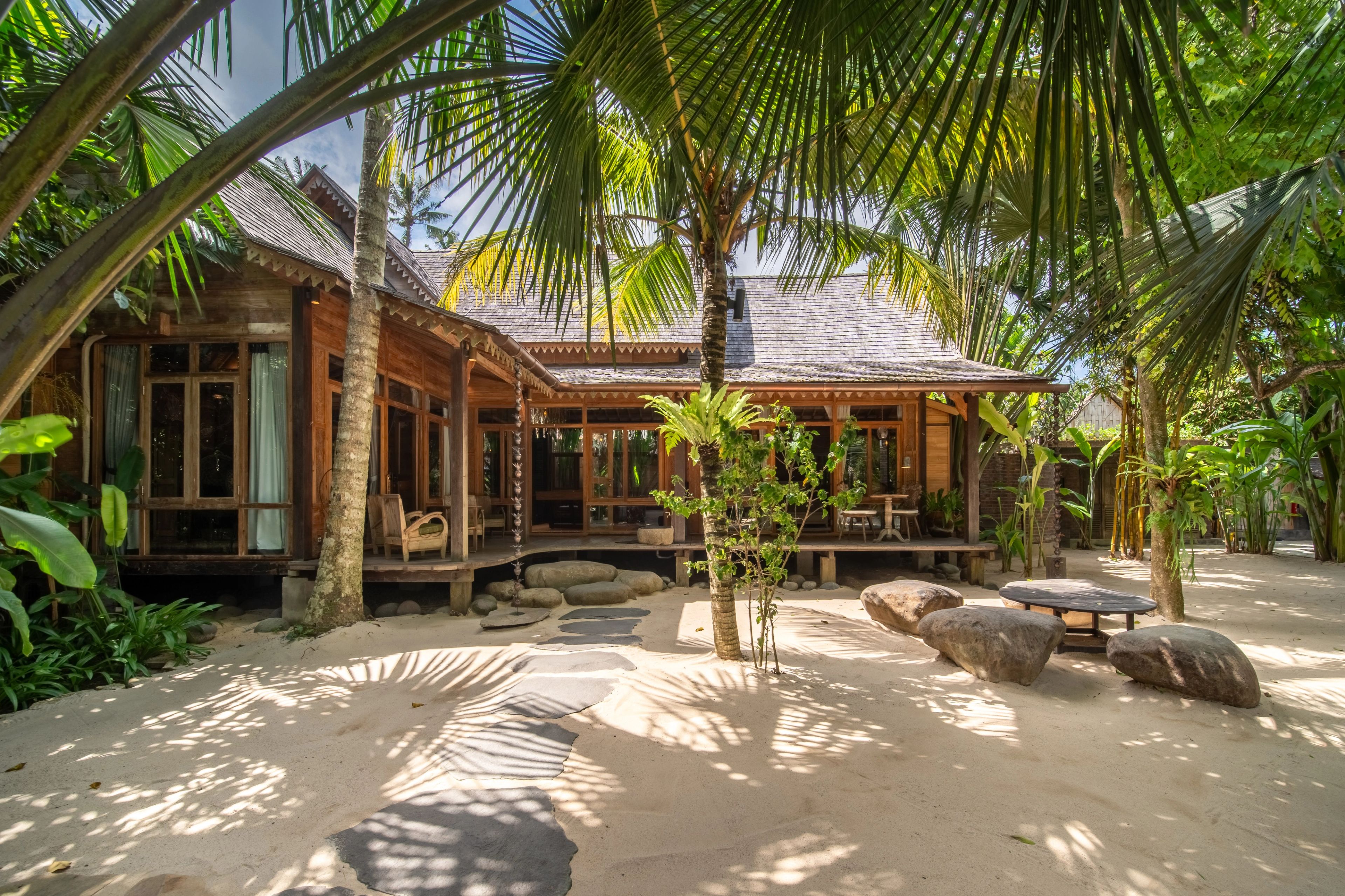 The villa wrapping around its sand courtyard, palms throwing shadows across it.