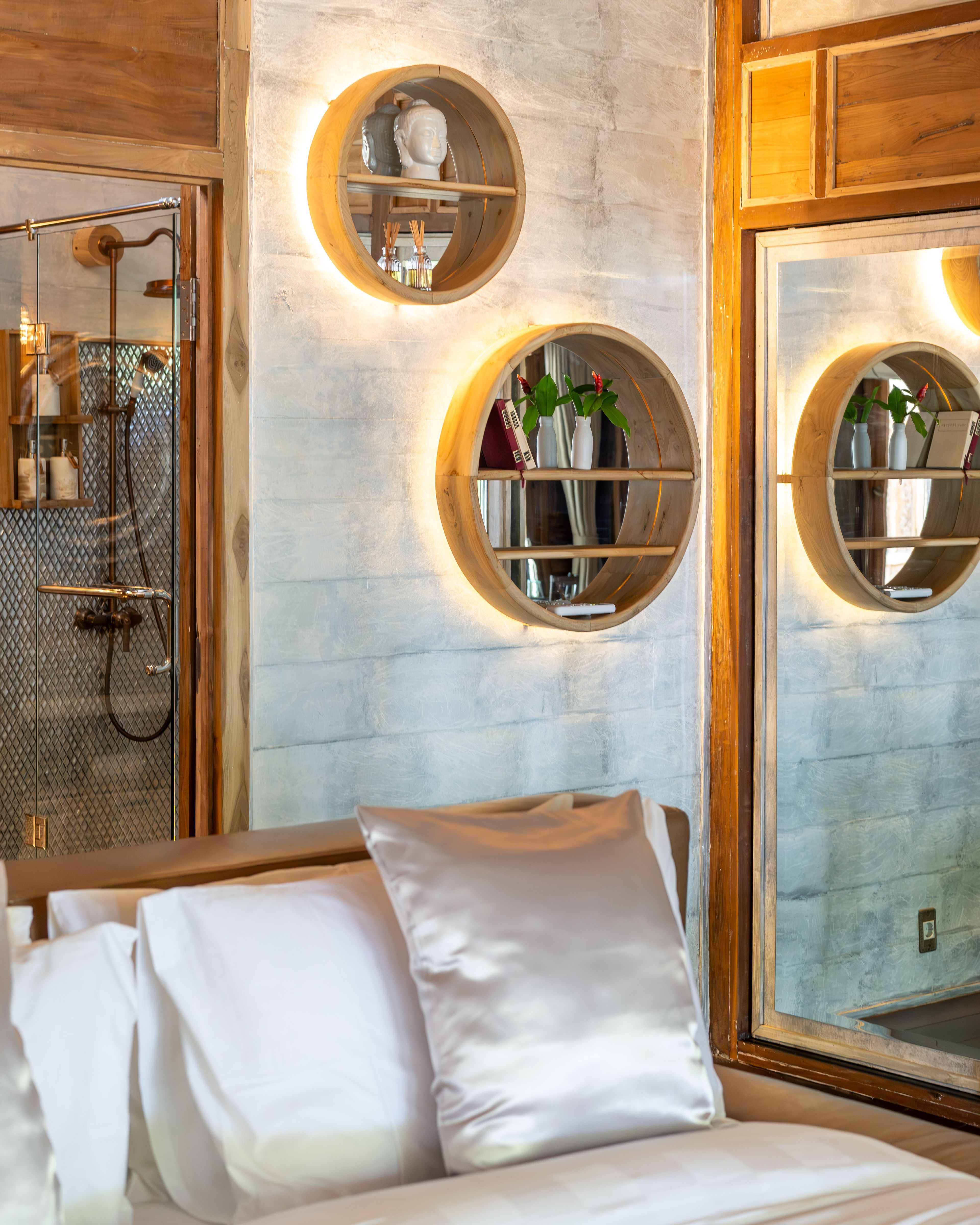 Round recessed shelves lit in the wall beside the shower, above the end of the bed.