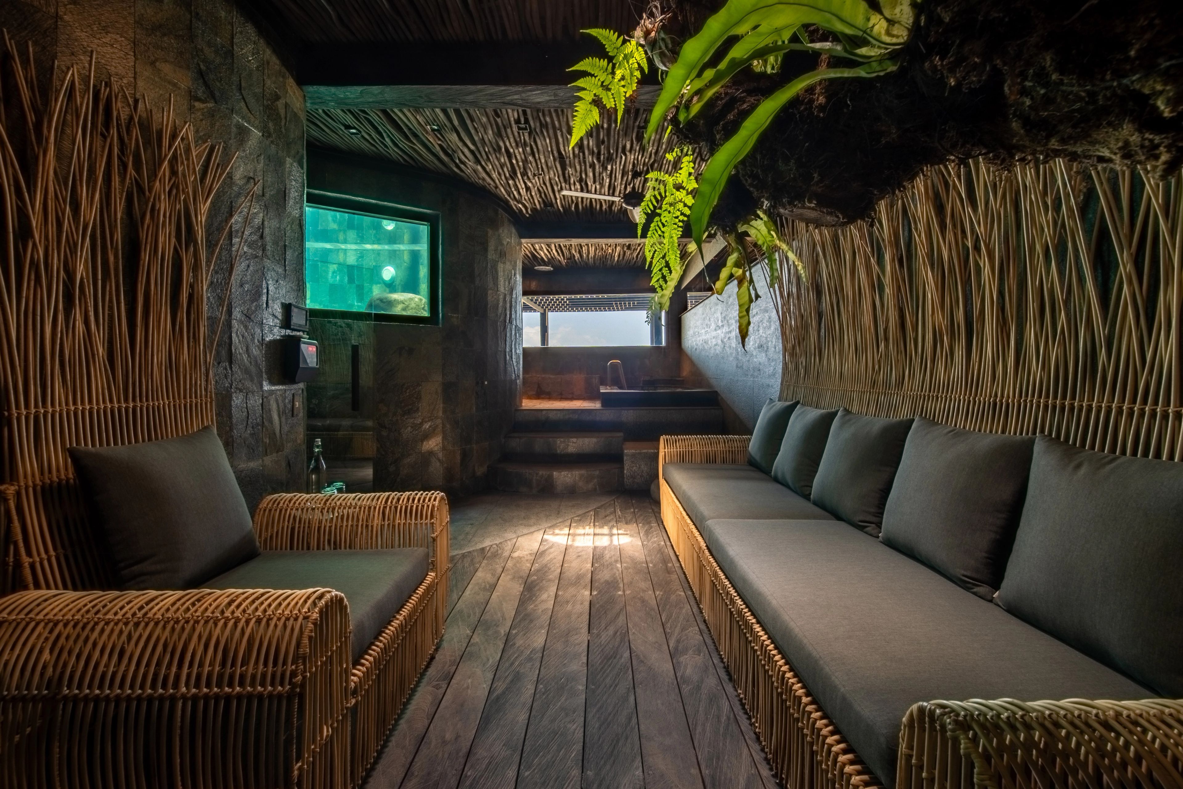 Rattan sofas facing each other down the spa lounge, planting overhead and an aquarium window glowing at the end.