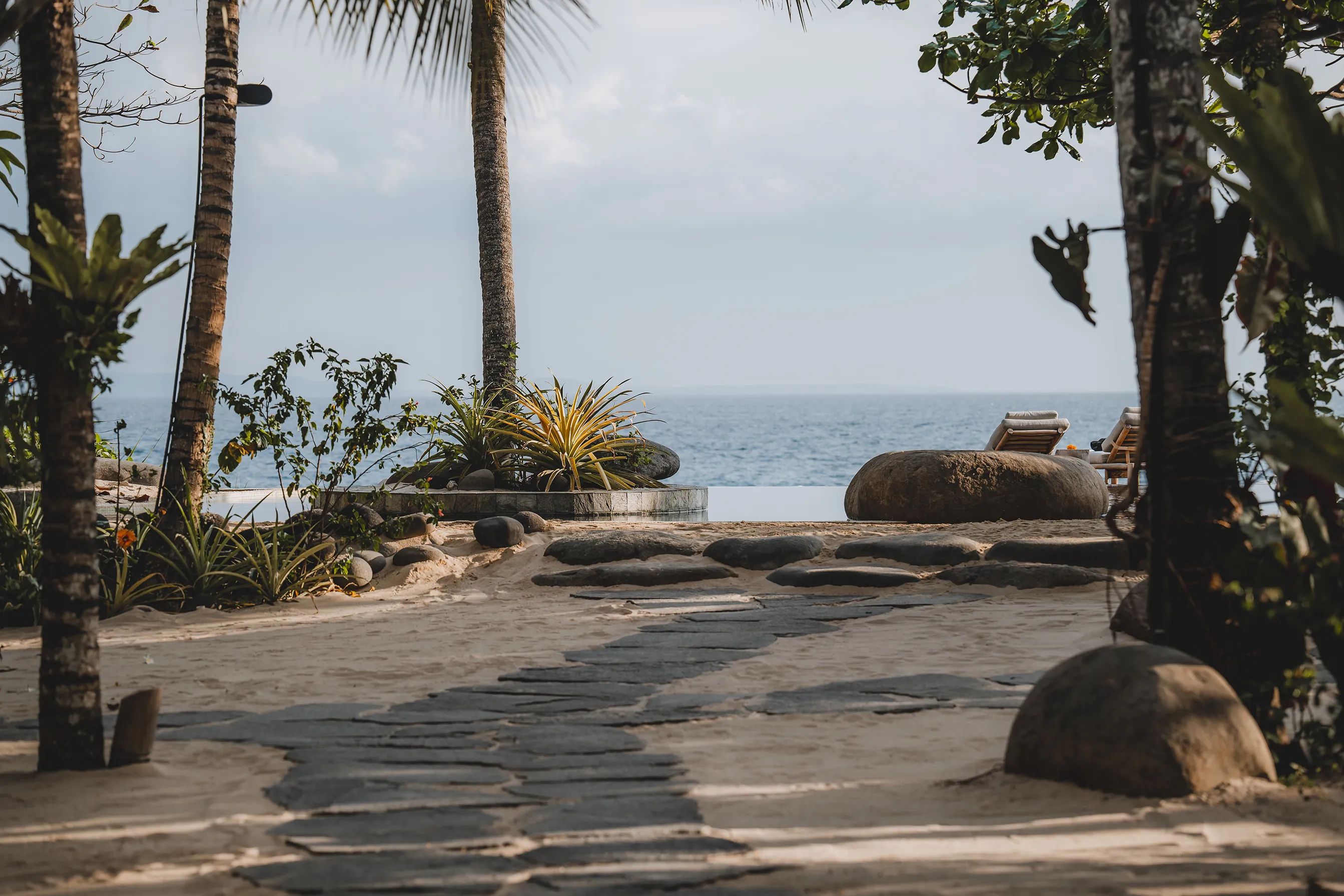 A stone path through the palms opening onto the pool terrace and the ocean beyond.