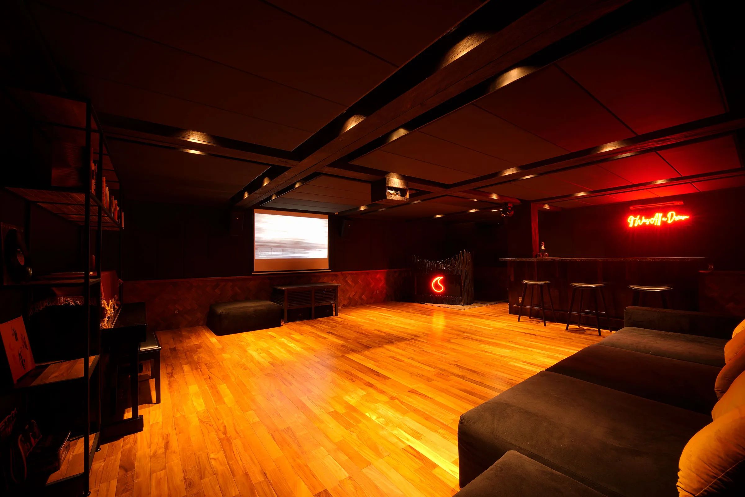 The basement club with its parquet floor lit warm, screen at one end and neon behind the bar.