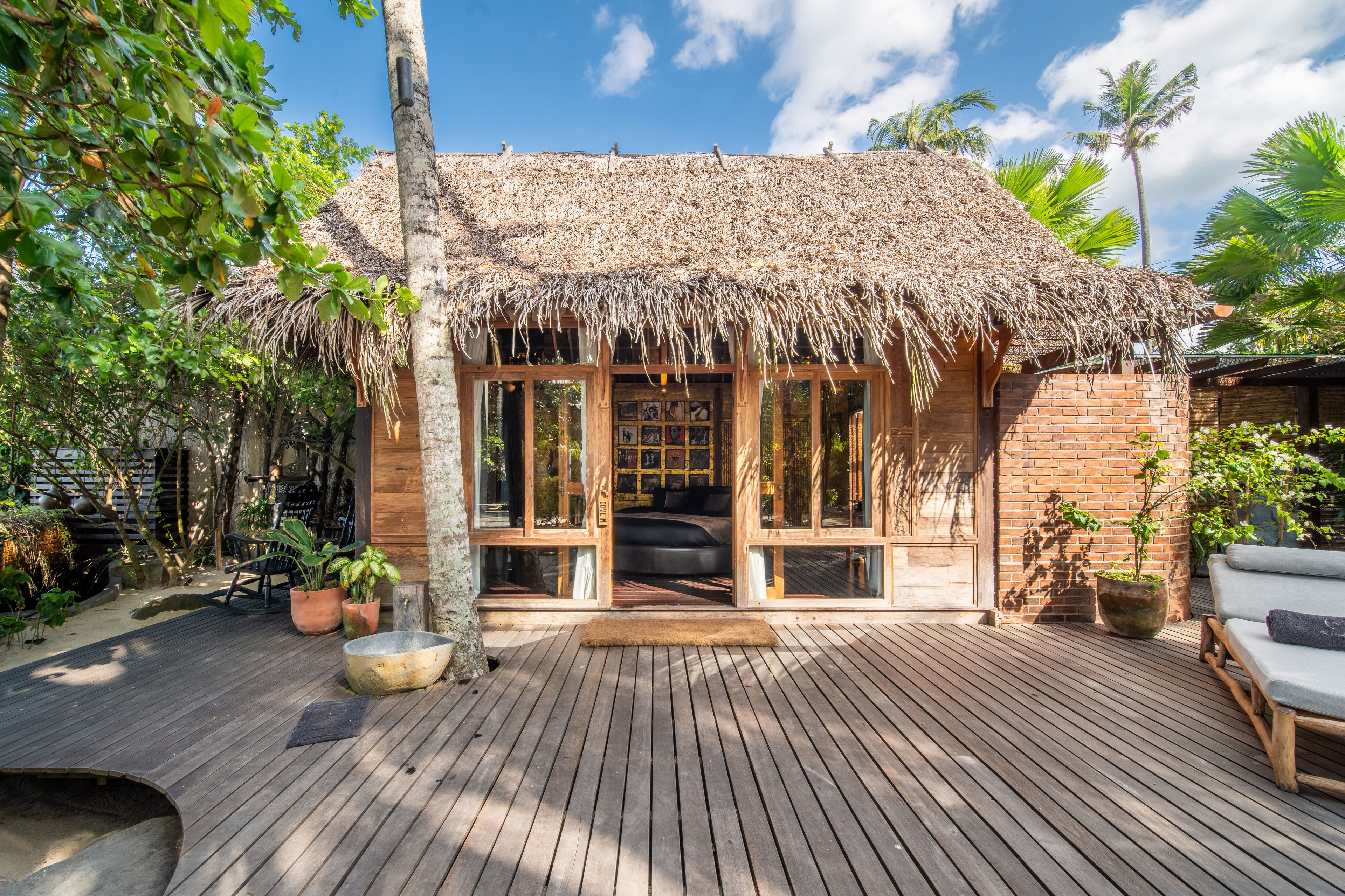 A thatched pavilion at the edge of the deck, loungers and planting either side under the palms.