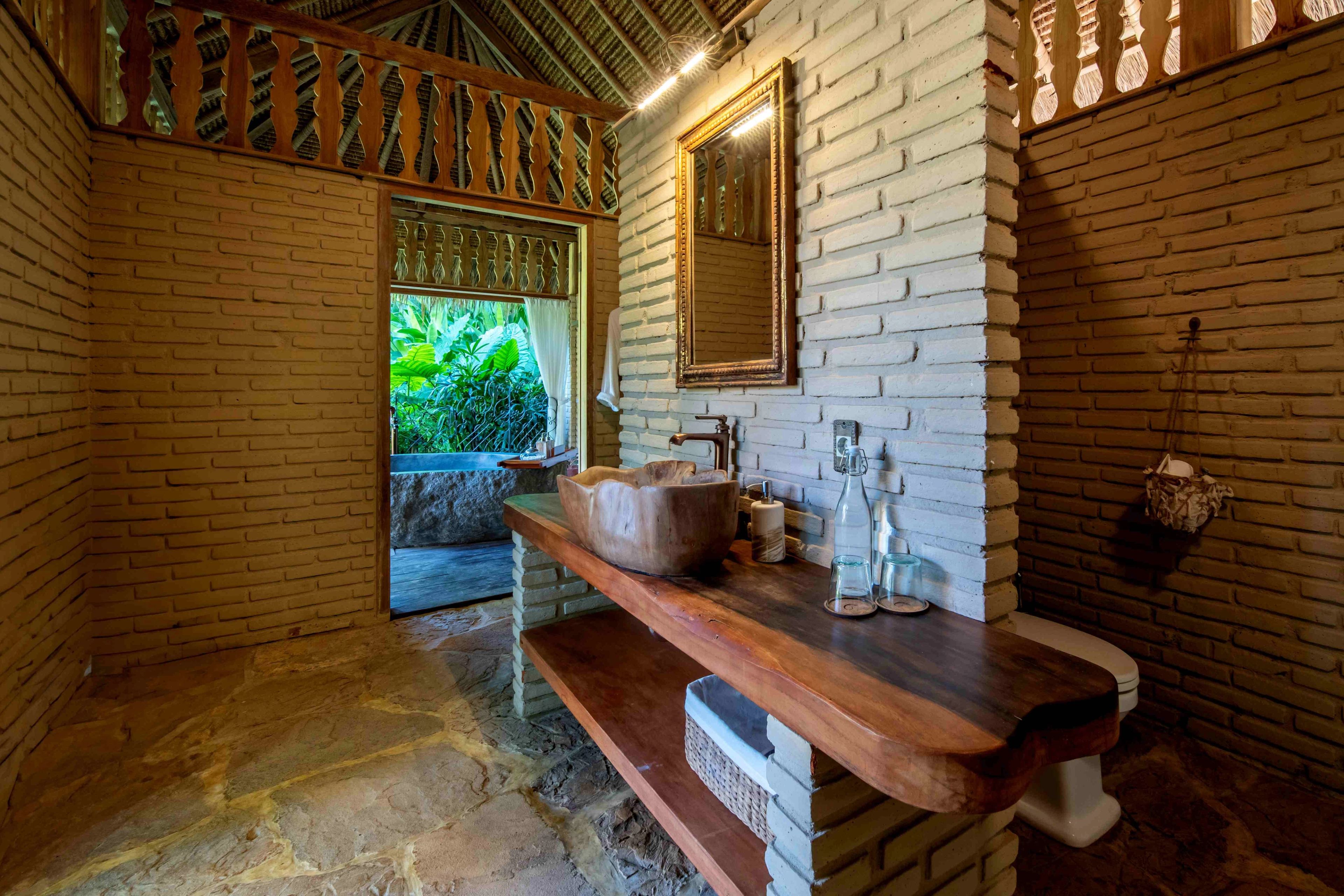 A stone basin on a live-edge timber washstand against a whitewashed brick wall, with a mirror above.