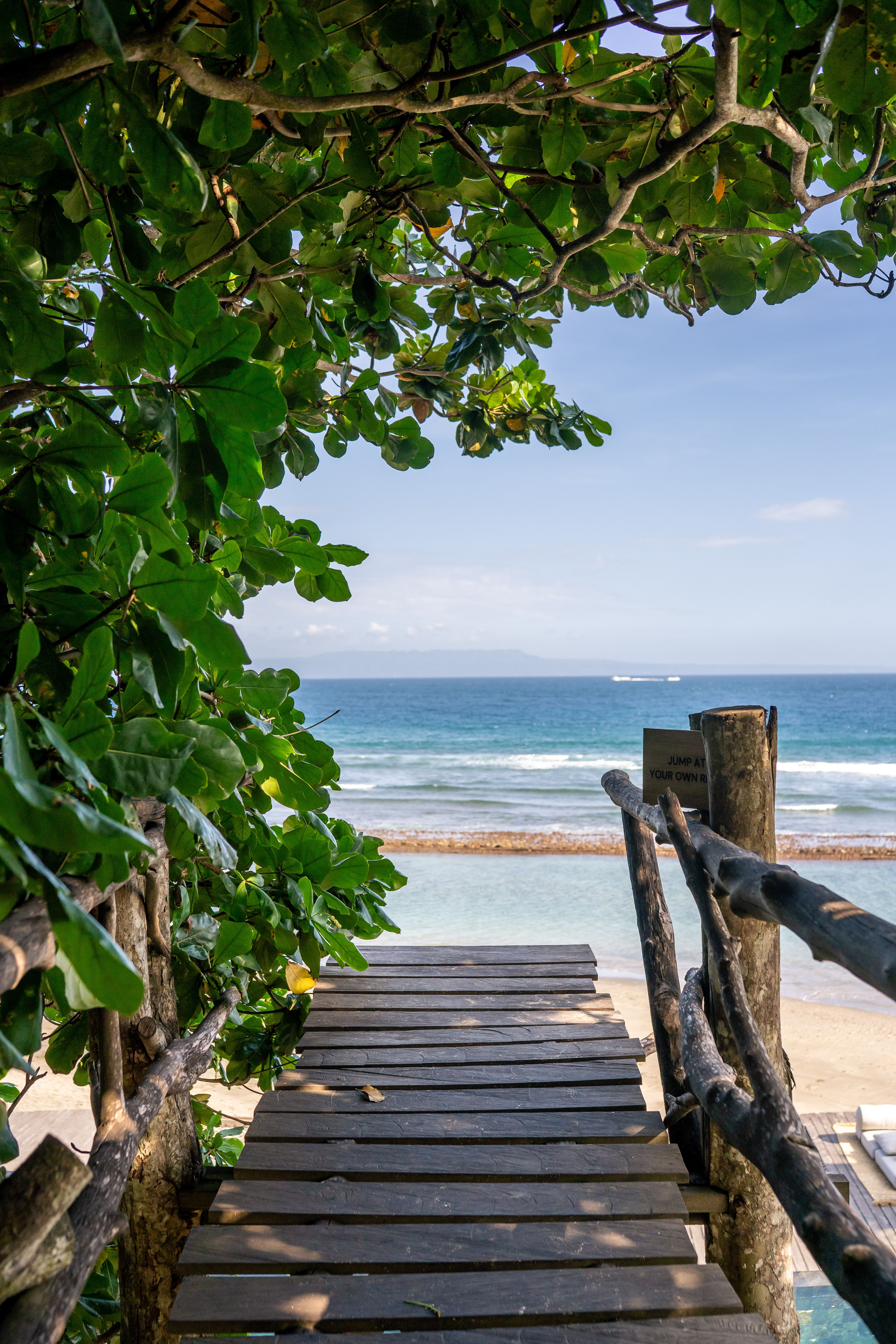The sand and surf framed by broad leaves and the timber rail of the walkway.