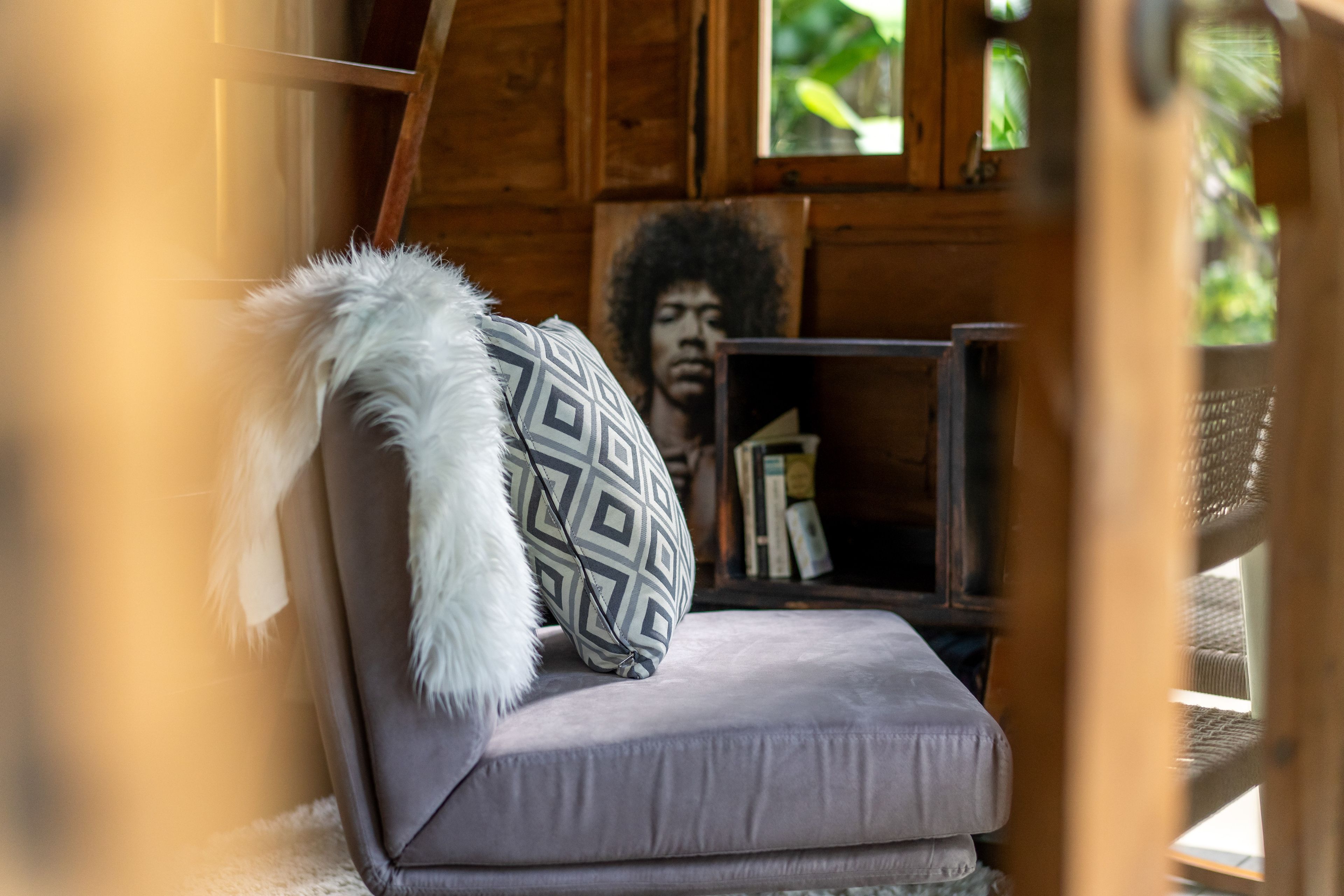 A grey armchair with a patterned cushion and throw, a framed portrait on the wall behind.