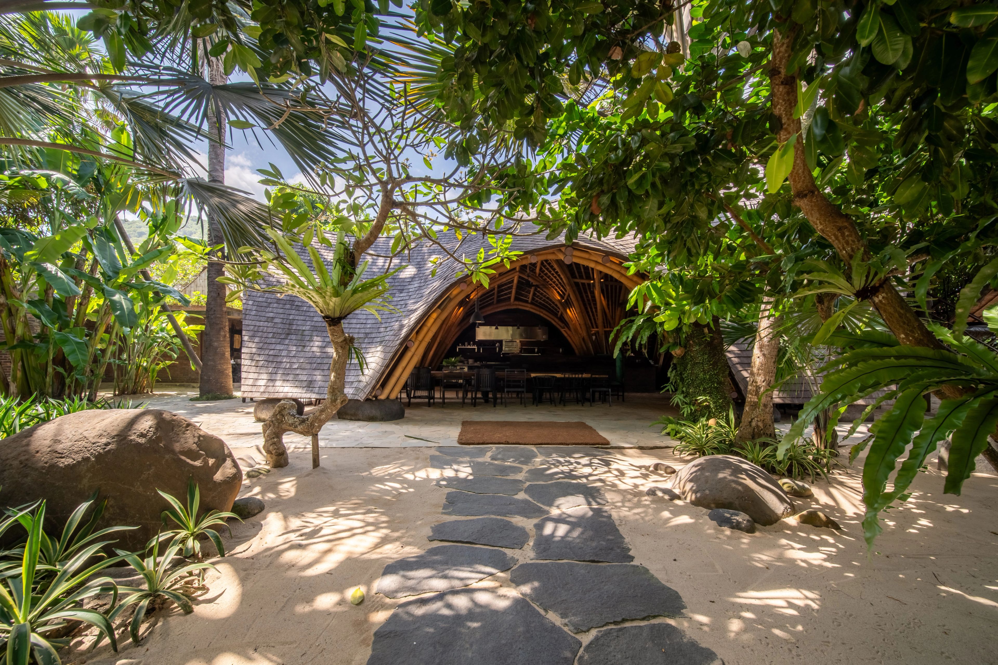 The curved bamboo entrance archway of the restaurant framed by tropical trees.