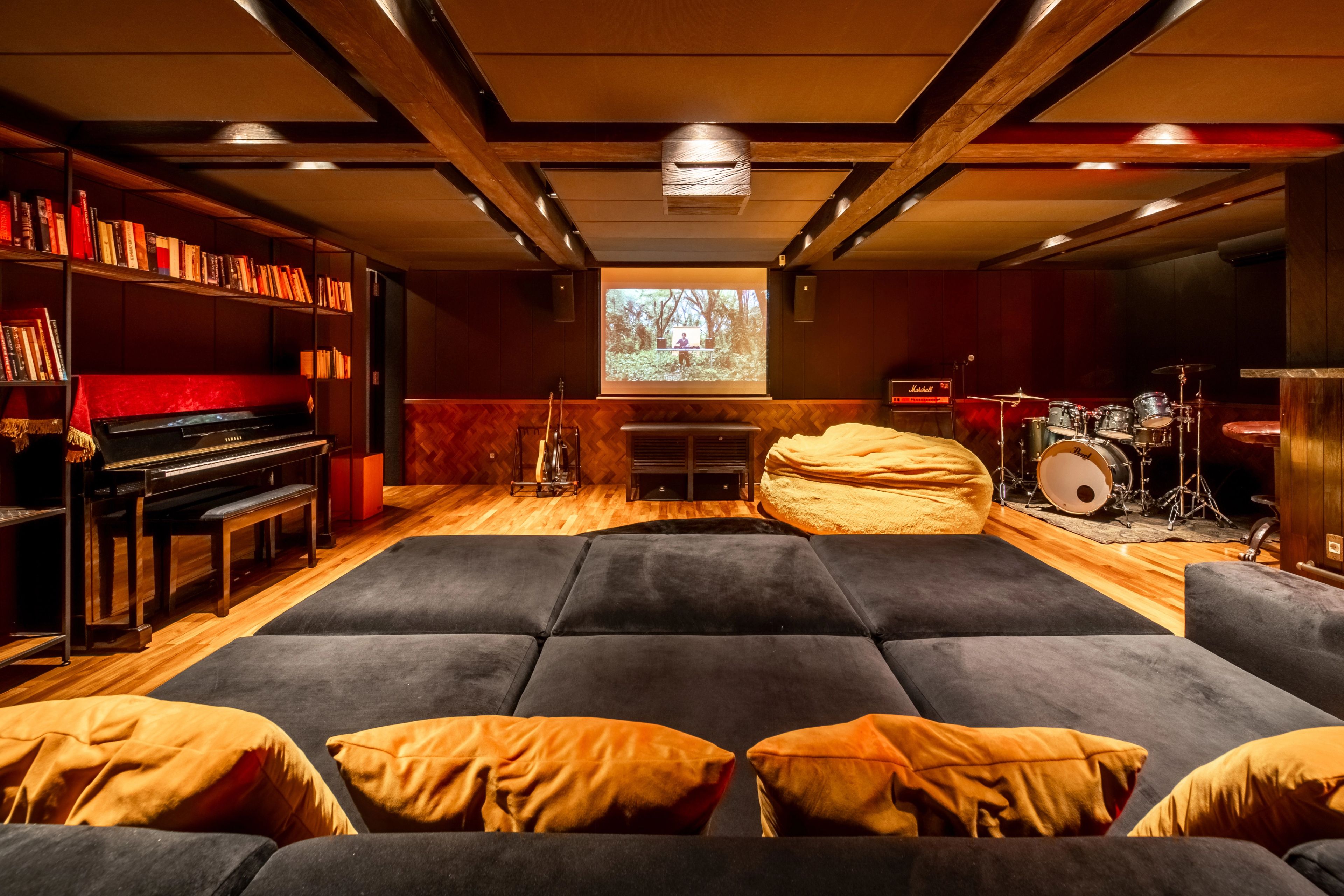 Floor cushions and mustard bolsters laid out before the screen, with the piano and drum kit either side.