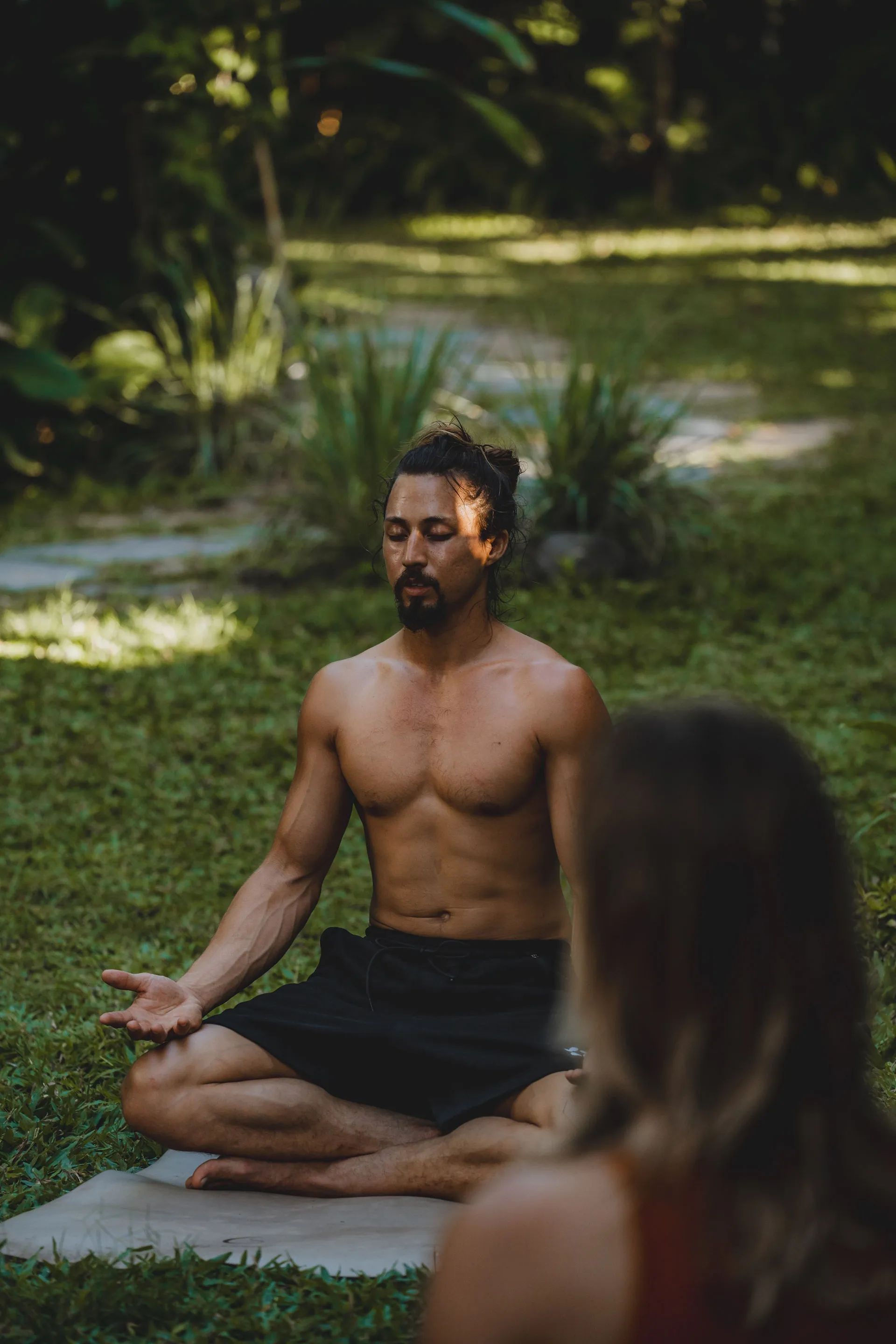 A man sitting upright on the grass with his eyes closed during a breathwork session.