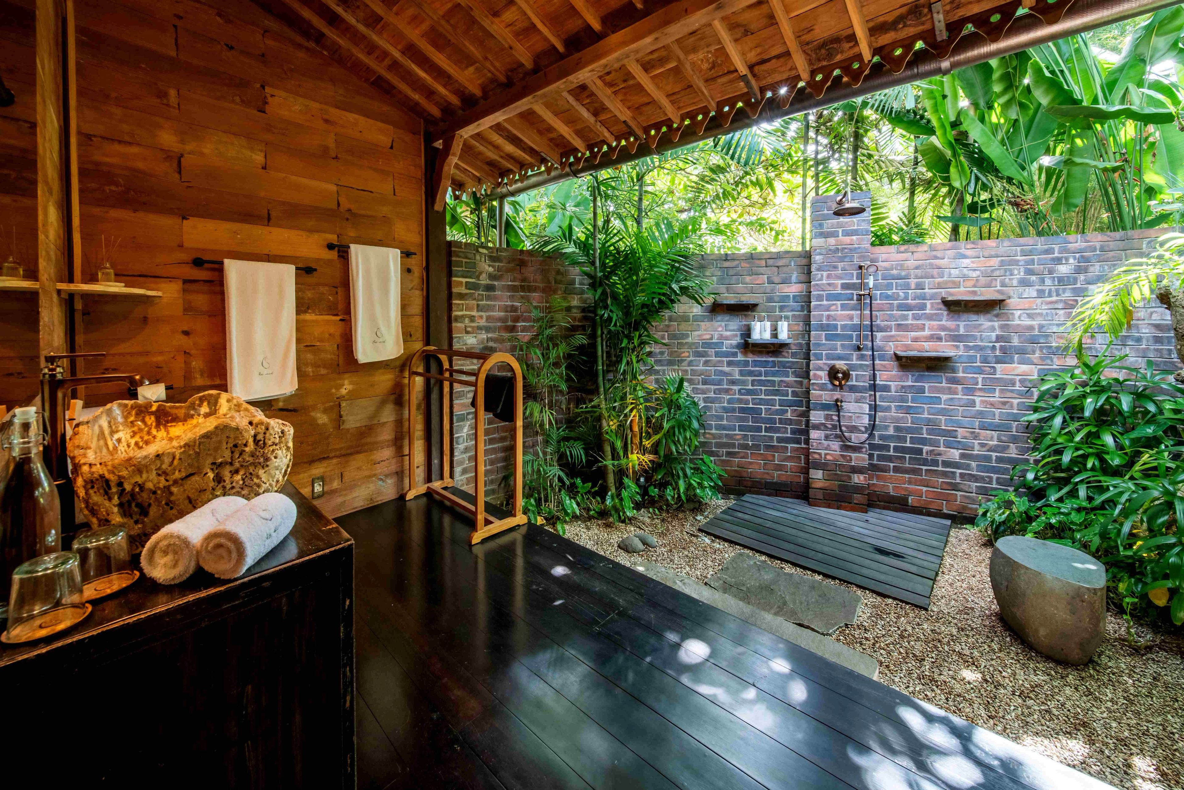 A timber bathroom counter opening onto a brick-walled garden shower.